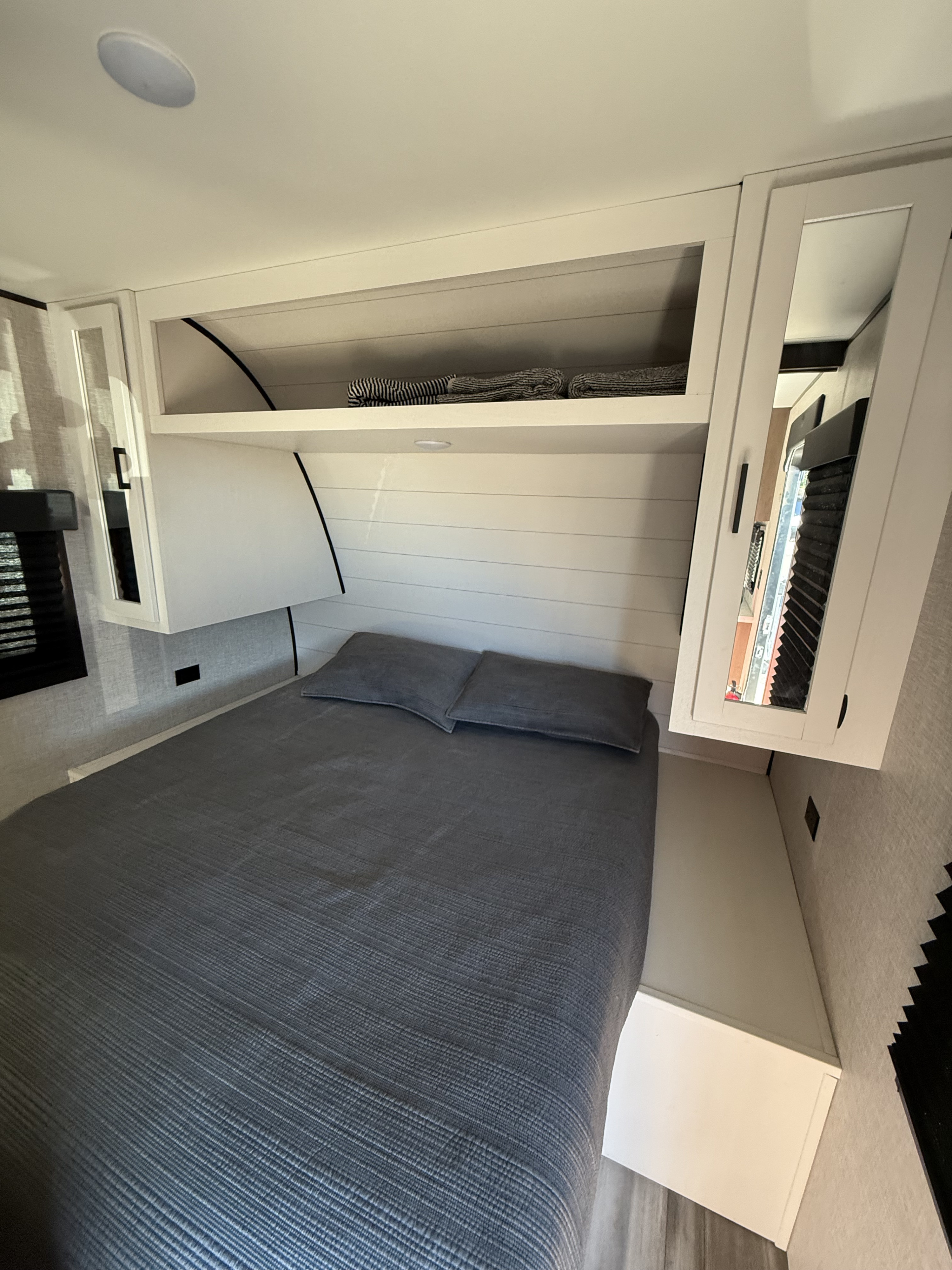 Compact RV rental bedroom features a gray bed, ample overhead storage, and modern paneling, designed for comfortable travel.. Starcraft Autumn Ridge 2024