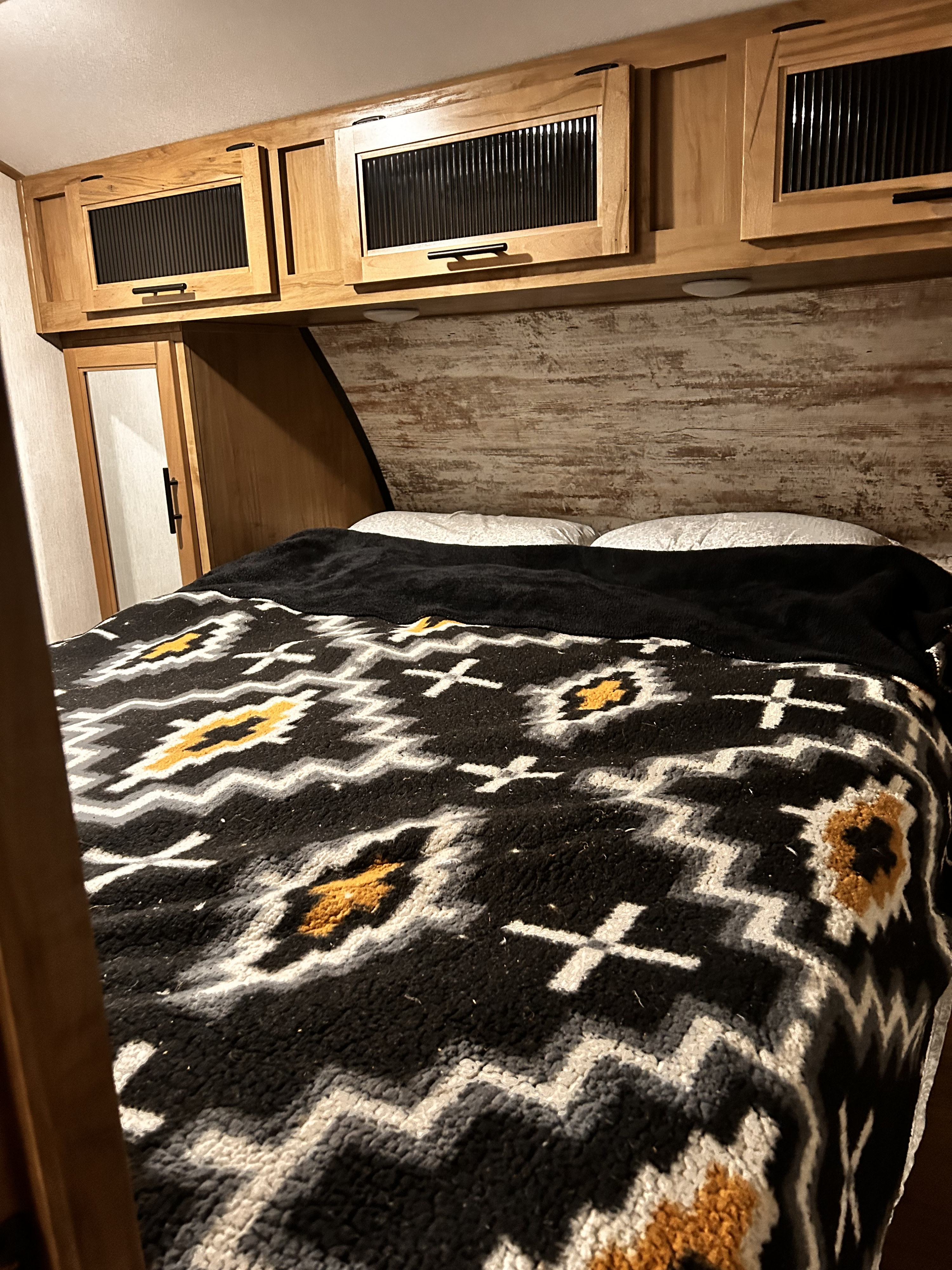 Cozy RV rental bedroom featuring a bed with a vibrant patterned blanket, rustic headboard, and overhead storage cabinets.. Forest River Cherokee Alpha Wolf DBH-L 2024