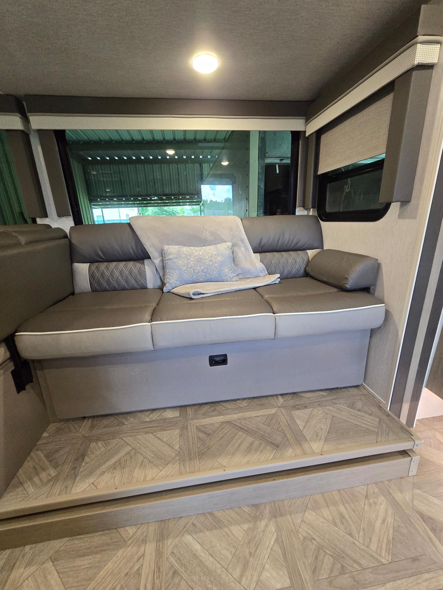Cozy RV rental interior: gray sofa with pillows, large window, and patterned wood-look flooring define this seating area.. Forest River Salem Cruise Lite Platinum 2023