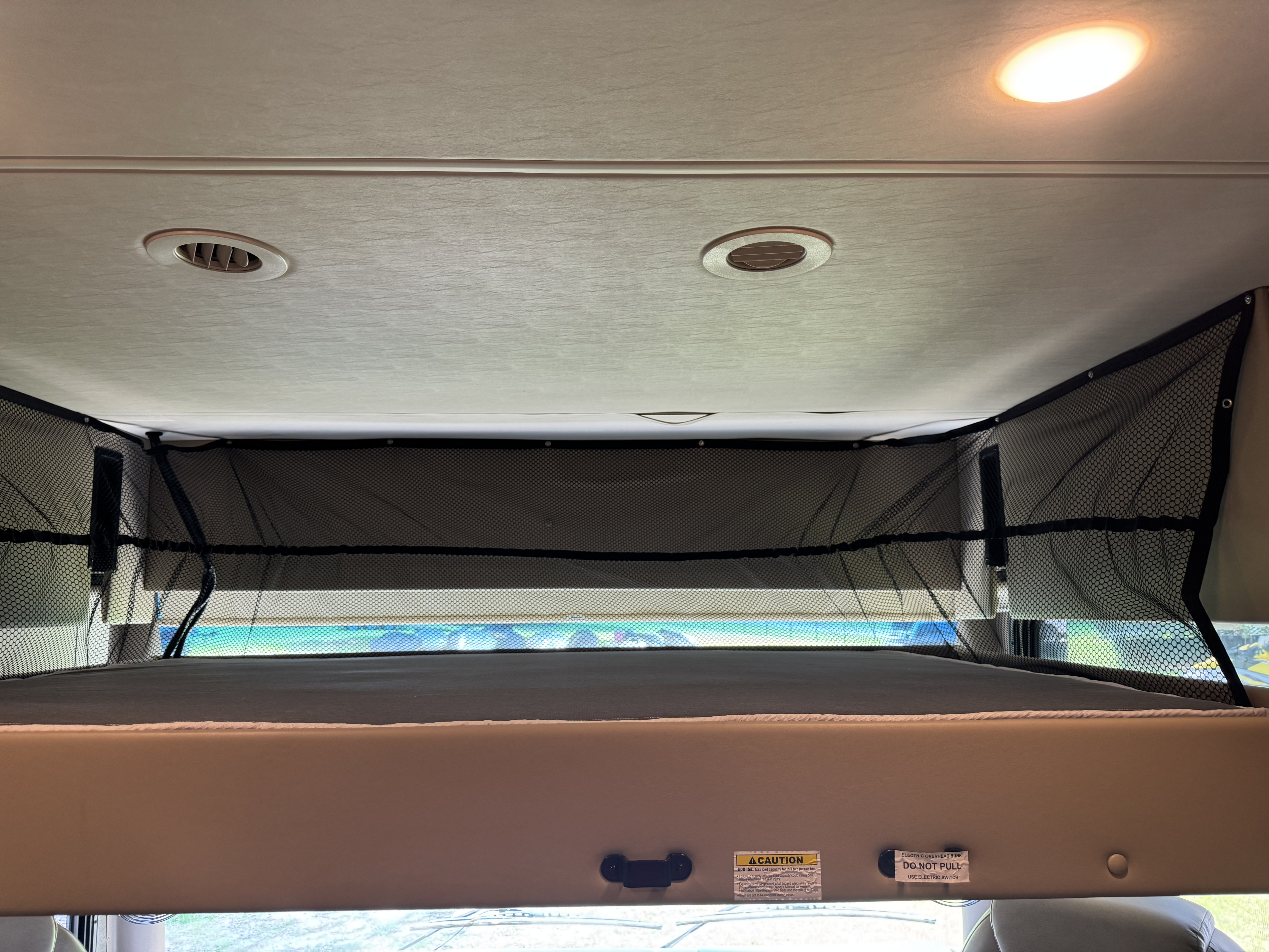 Overhead bunk bed with safety net in an RV rental, showing 500 lbs. weight capacity and electric switch warnings.. Thor Challenger 2020