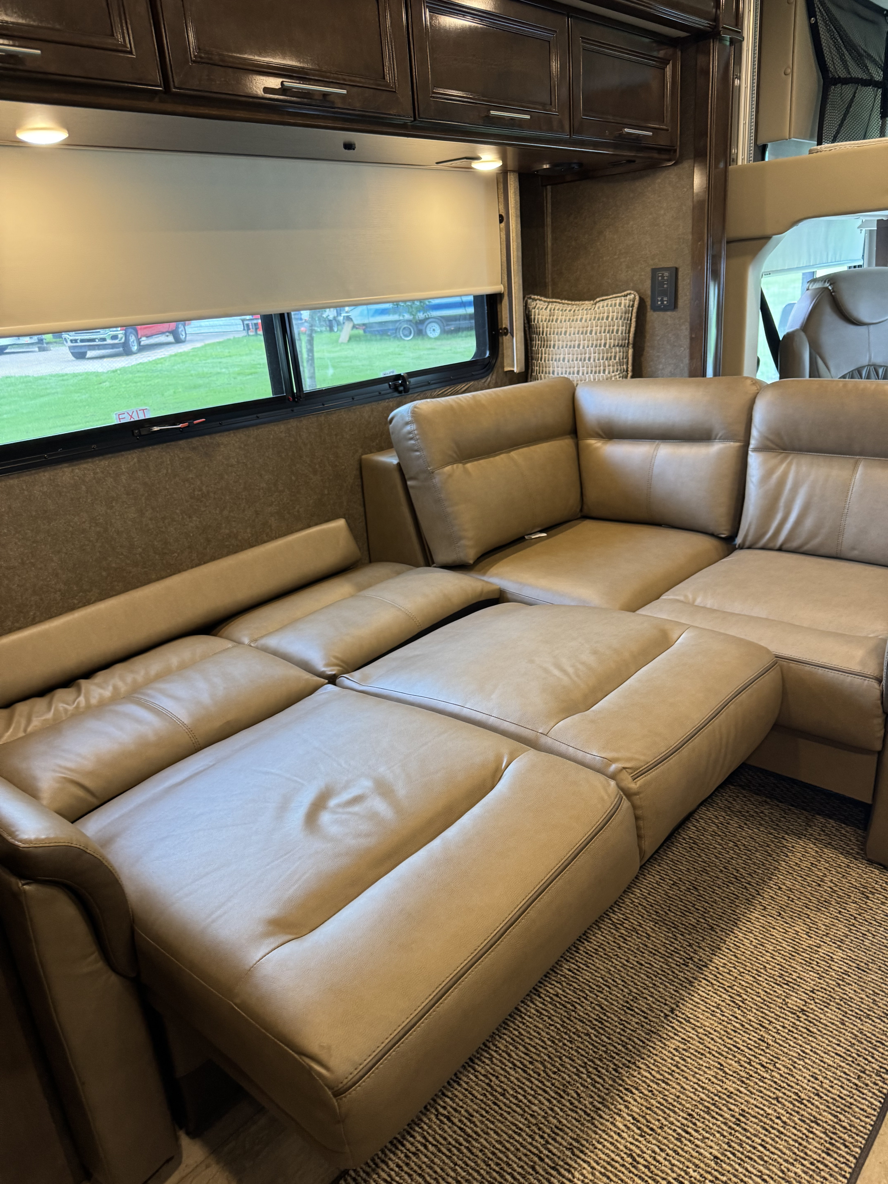 This RV rental's living space features a large, light brown leather sectional with extended recliners and overhead cabinets.. Thor Challenger 2020