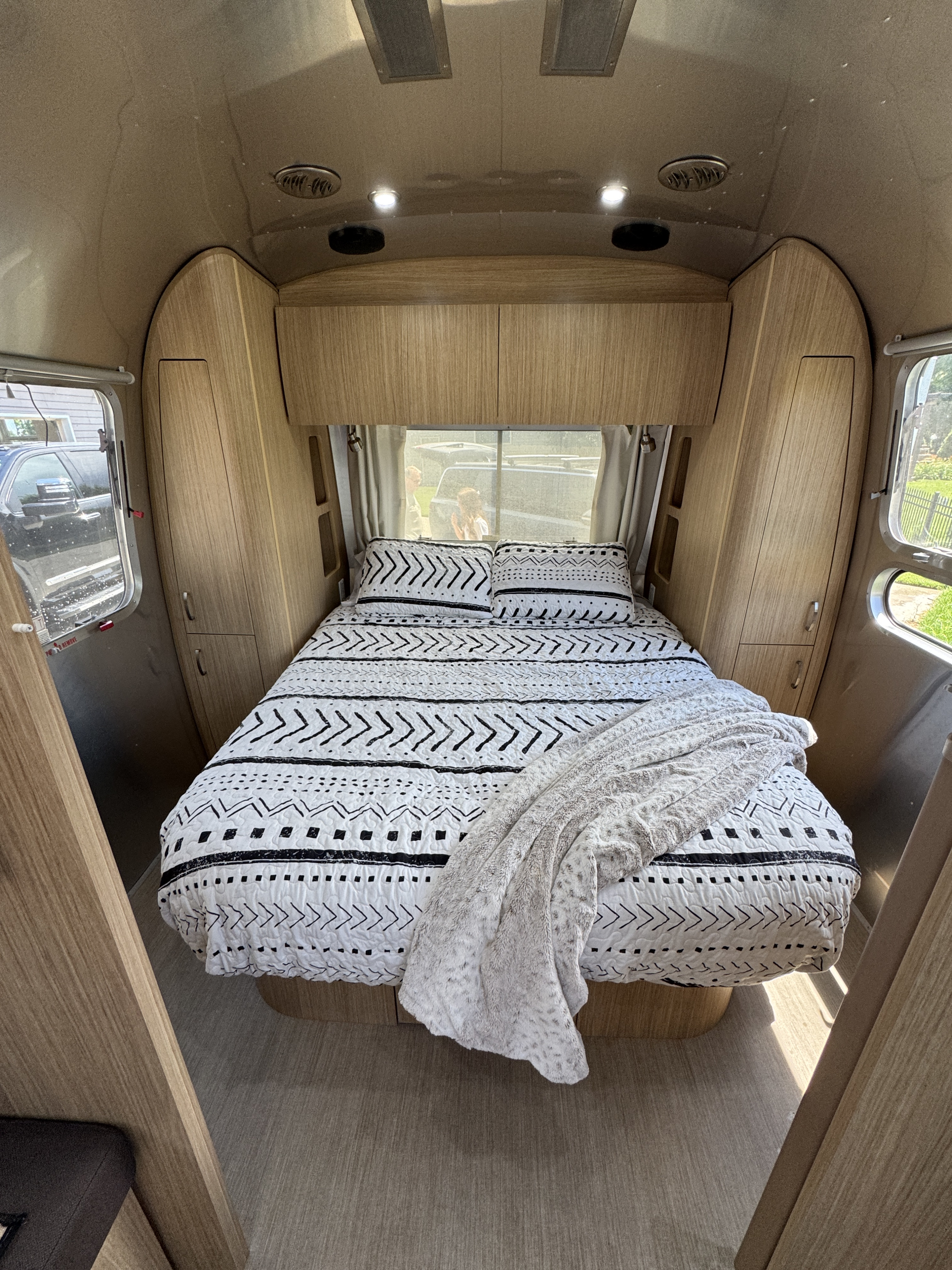 Inside an RV rental: a cozy bedroom features a bed with patterned bedding & wooden cabinetry.. Airstream Flying Cloud 2018
