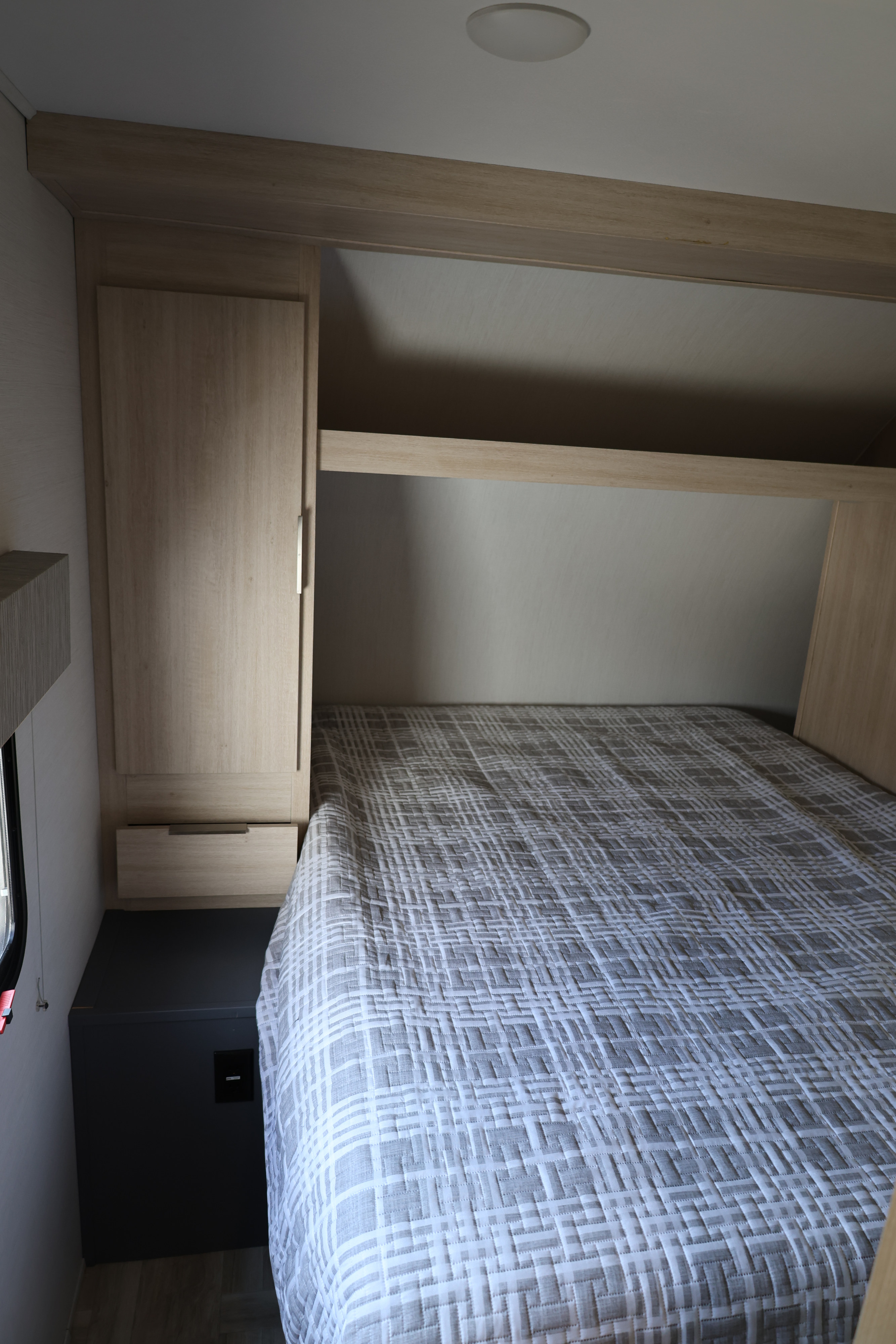 Compact RV rental bedroom featuring a patterned bed, modern overhead storage, and light wood cabinetry.. Forest River Tracer 28BHS 2024