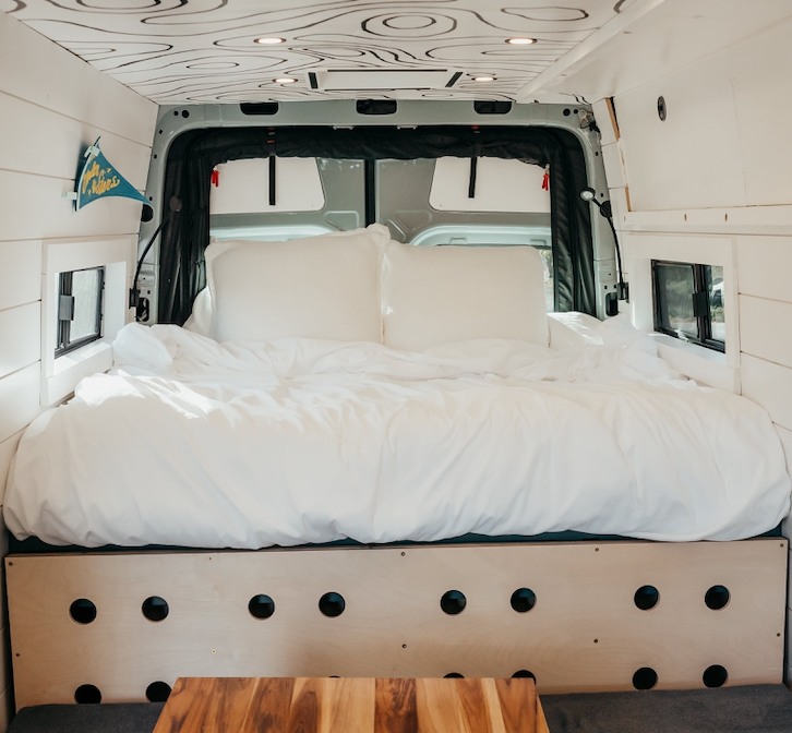 Comfortable RV rental interior: a large bed with white bedding, white walls, small windows, and a map-patterned ceiling.. Mercedes-Benz Sprinter 2022