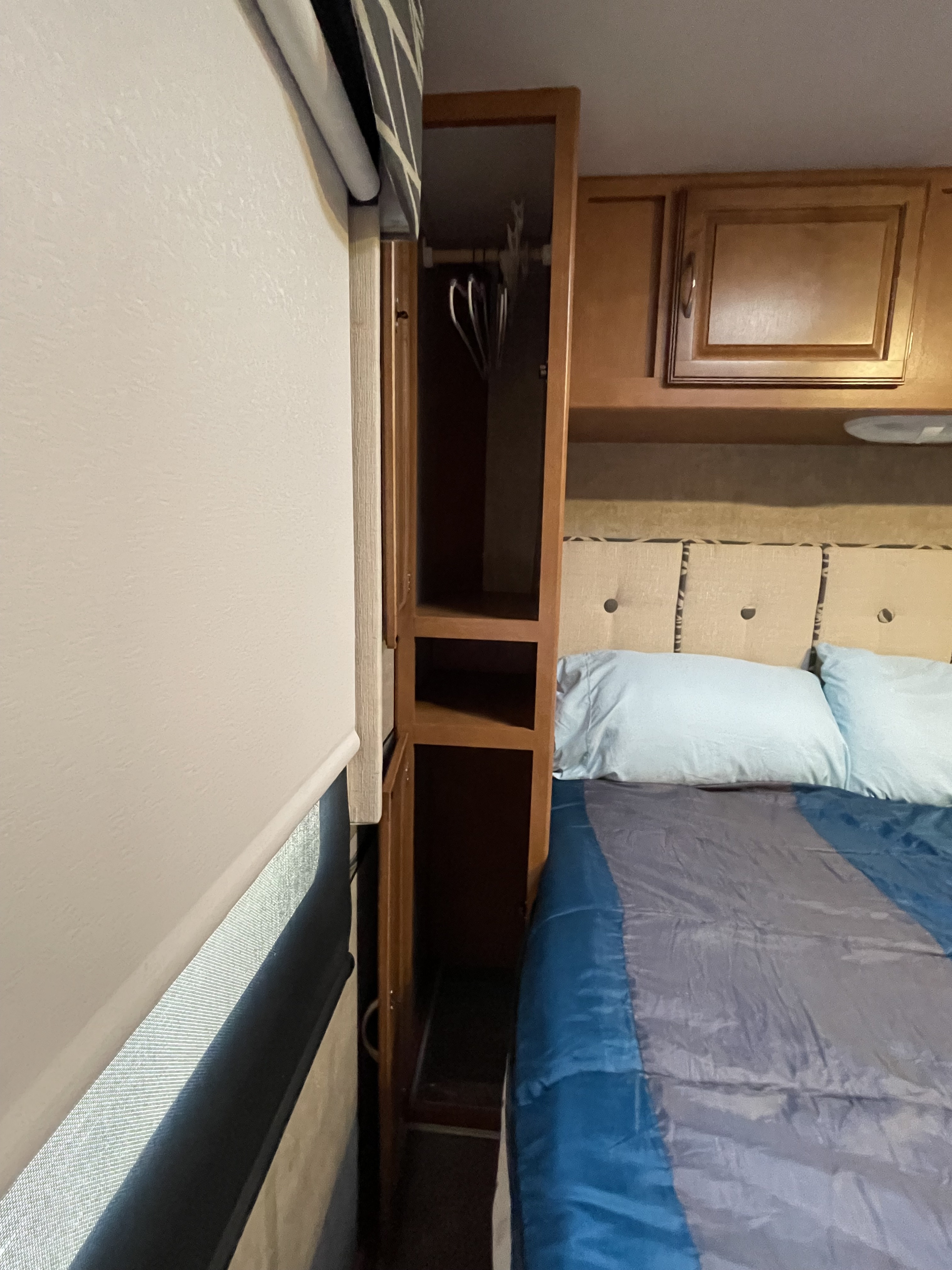 RV rental bedroom interior: light walls, open wooden closet, bed with blue/grey bedding, and padded headboard for comfort.. Winnebago Minnie Winnie 2017