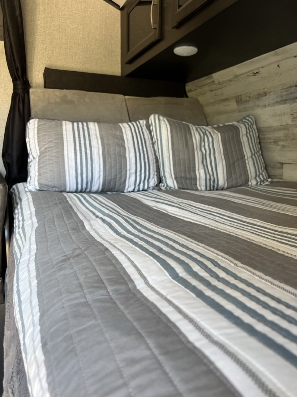 Cozy RV rental bedroom featuring gray & white striped bedding, pillows, & built-in cabinets. Ideal for travel comfort.. Jayco Jay Feather Micro 2021