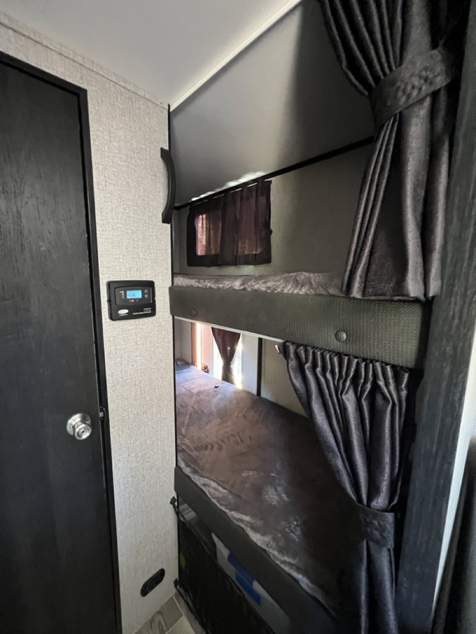 RV rental interior showing a compact sleeping area with two stacked bunk beds, dark privacy curtains, and a control panel.. Jayco Jay Feather Micro 2021