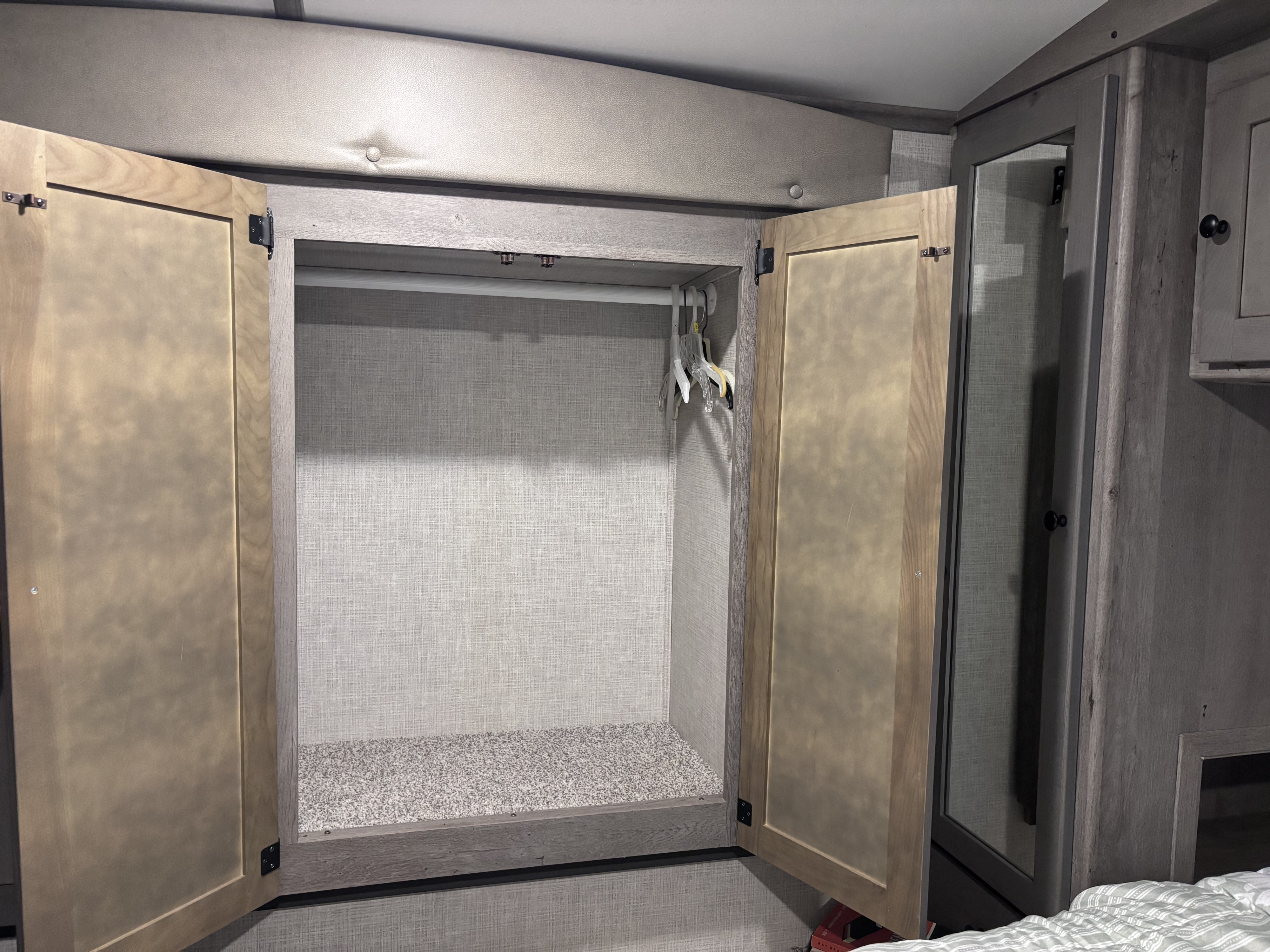 Compact RV rental wardrobe with open doors, hanging rod, and carpeted base. Ideal storage for travel.. Keystone RV Outback 2020