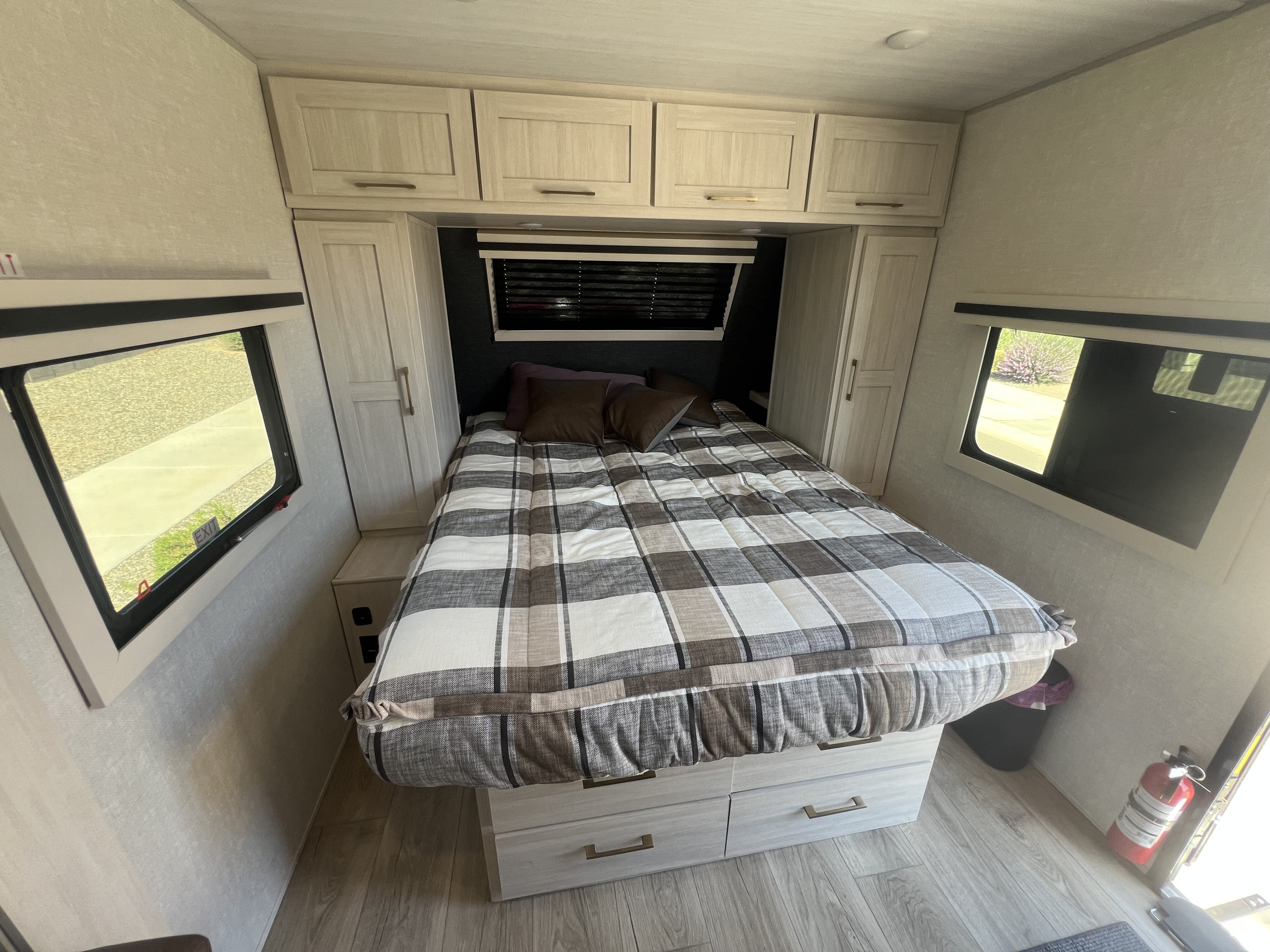 This RV rental bedroom offers a cozy bed with plaid comforter, integrated storage, windows, and essential amenities.. Forest River Surveyor 2025