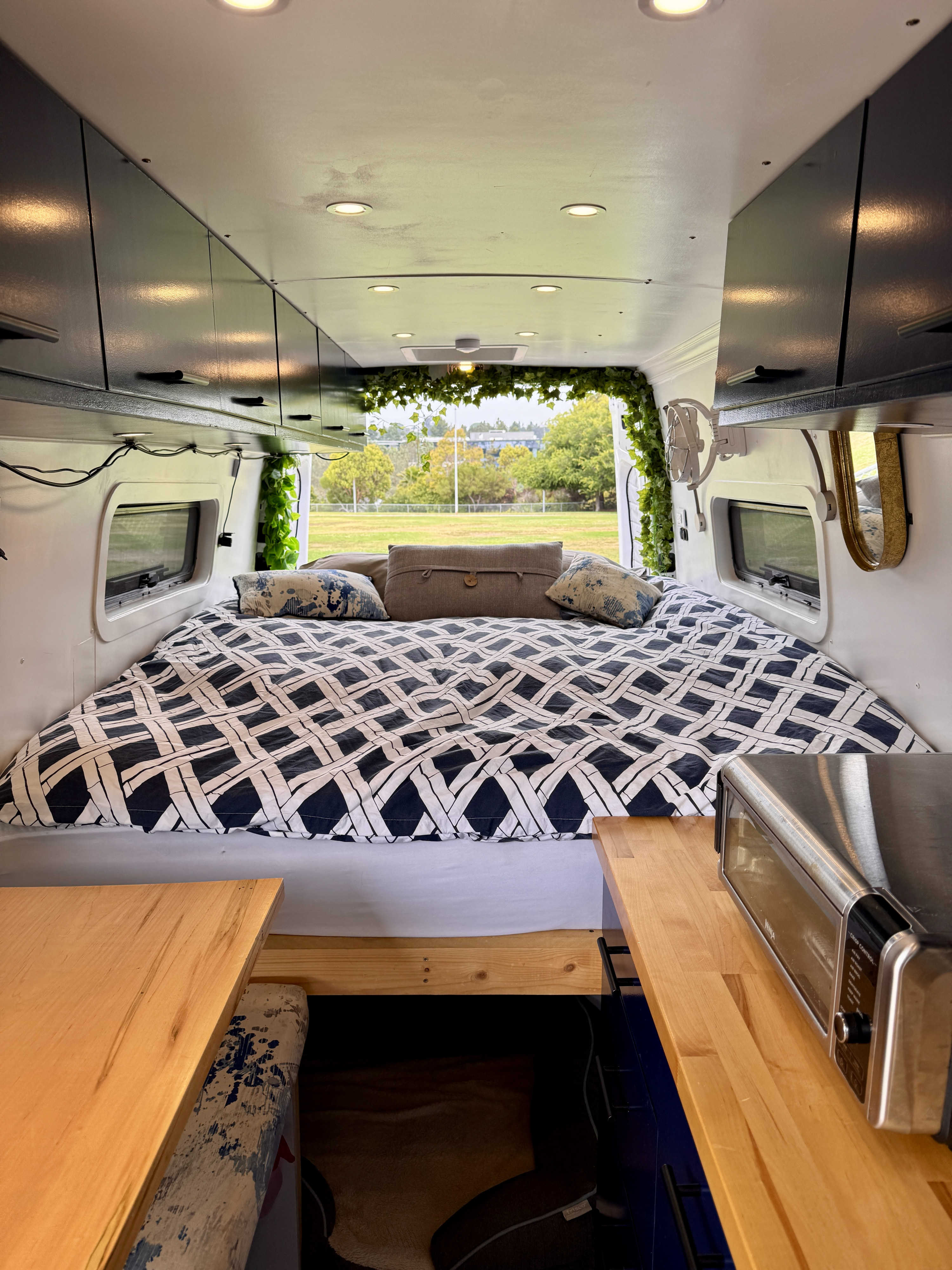 Modern RV rental interior: cozy bed, overhead cabinets, kitchen area with toaster, and leafy green decor. Ready for adventure!. Mercedes-Benz Sprinter 2020