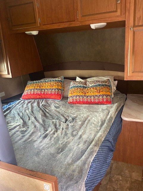 Cozy RV rental bedroom featuring a comfortable bed with colorful pillows, a plush grey blanket, and ample overhead storage.. Jayco Jay Flight 2013