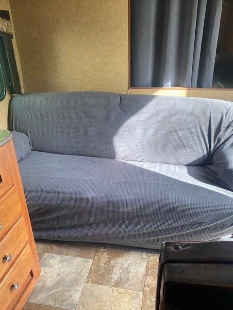 View inside an RV rental showing a grey slipcovered sofa, wood dresser, and tiled floor, illuminated by sunlight.. Jayco Jay Flight 2013