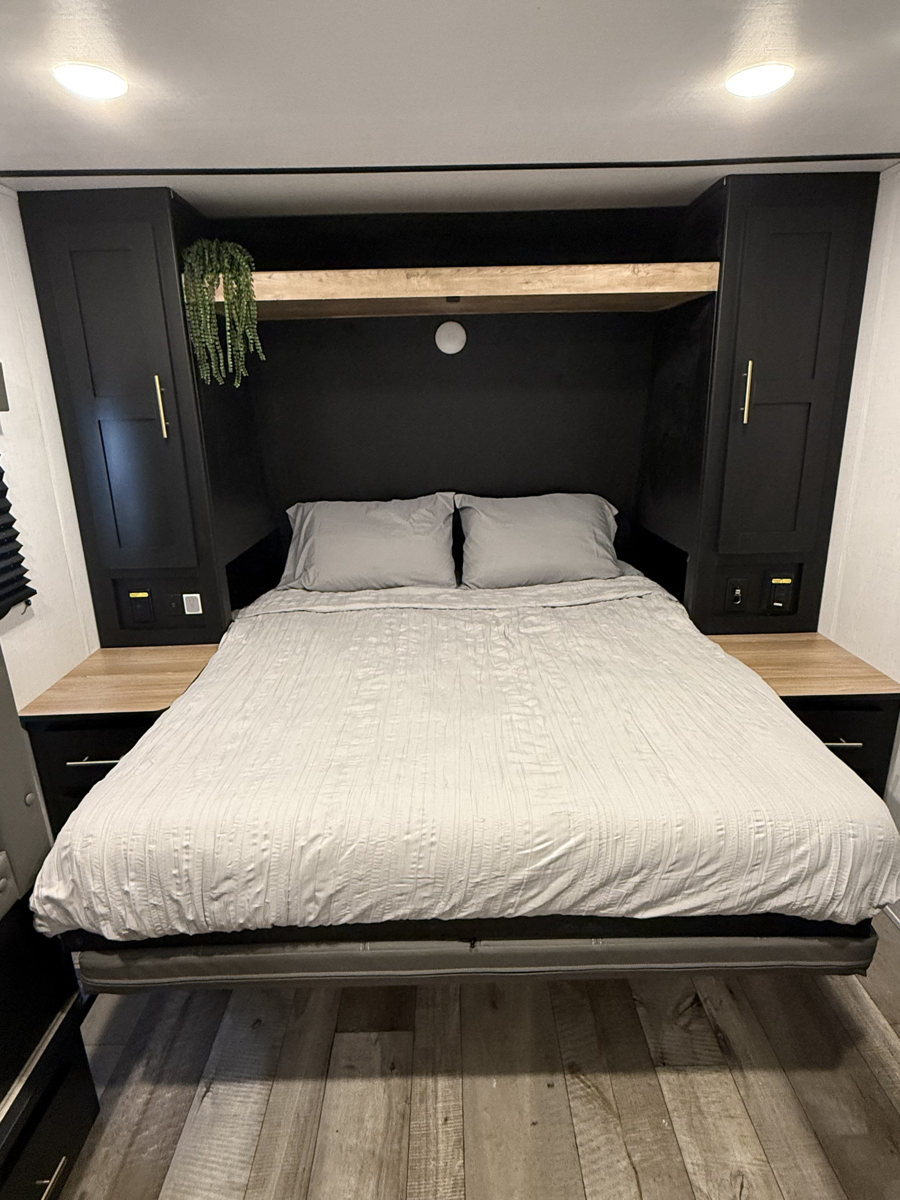 Modern RV rental bedroom with a comfortable bed, sleek black cabinets, wooden accents, and good lighting.. Keystone RV Springdale 2023