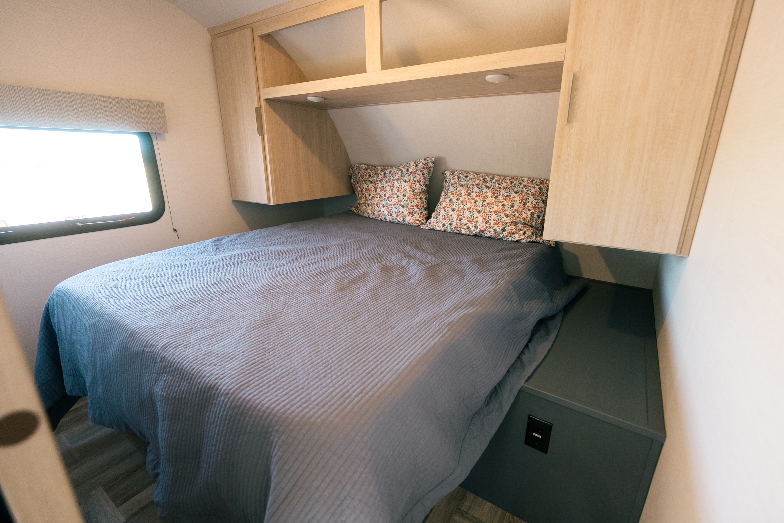 Cozy RV rental bedroom with a comfy bed, floral pillows, wood cabinets, and window. Ideal for travel.. Prime Time Tracer 270BHSLE 2024