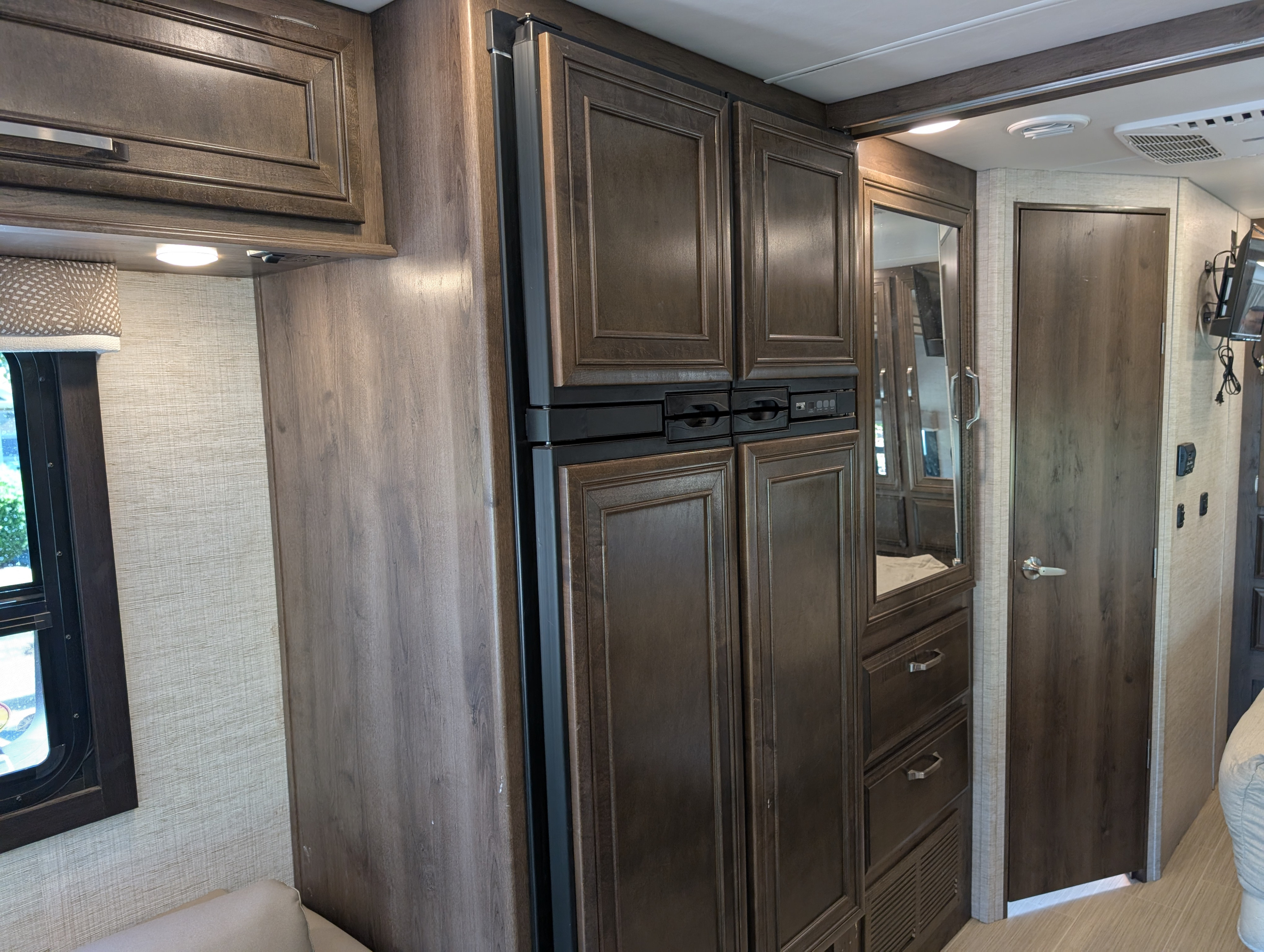 RV rental interior: Dark wood-look cabinetry, built-in refrigerator, mirrored wardrobe, and textured walls define this mobile living space.. Entegra Coach Esteem 2021