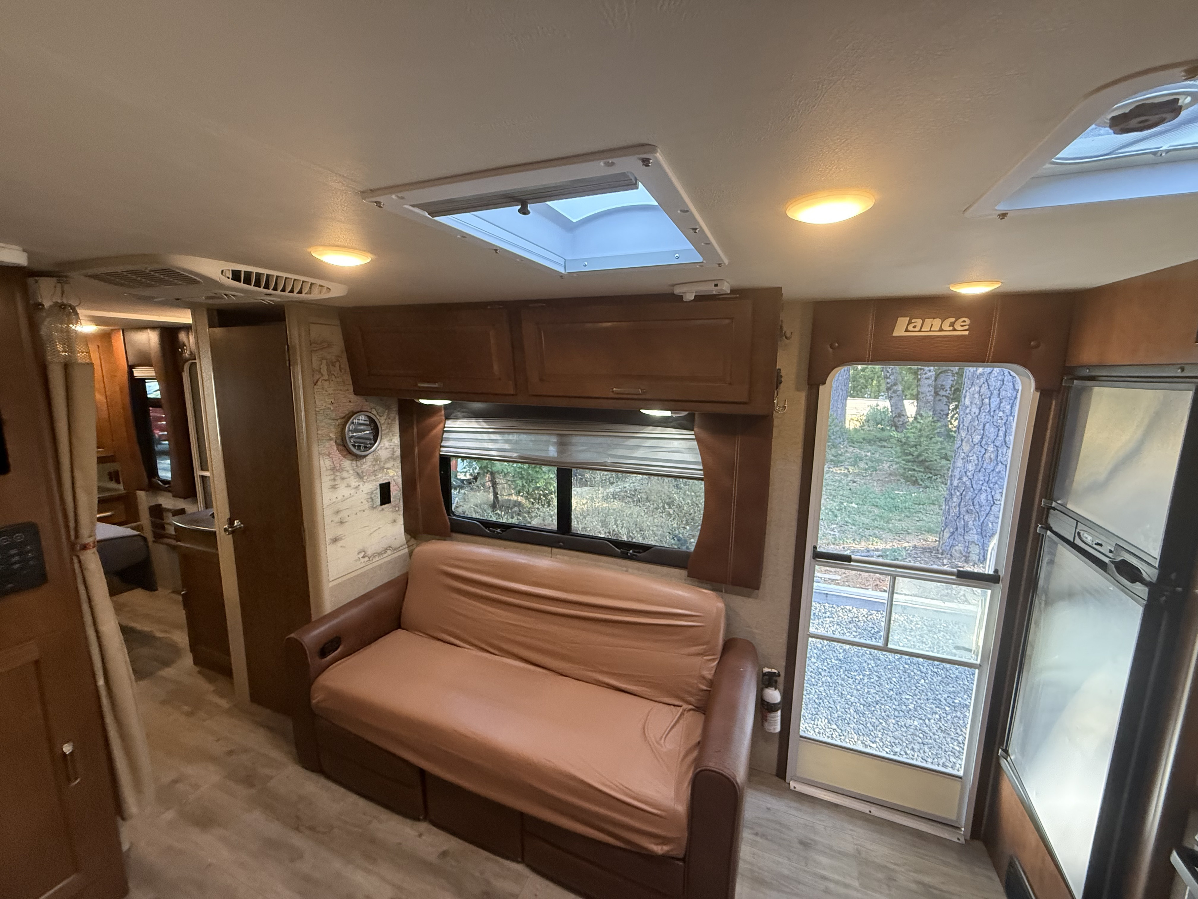 Comfortable RV rental interior: living area with sofa, large window, small fridge, and a hallway leading to the back.. Lance Manufacturing Lance Manufacturing Trailer 2018