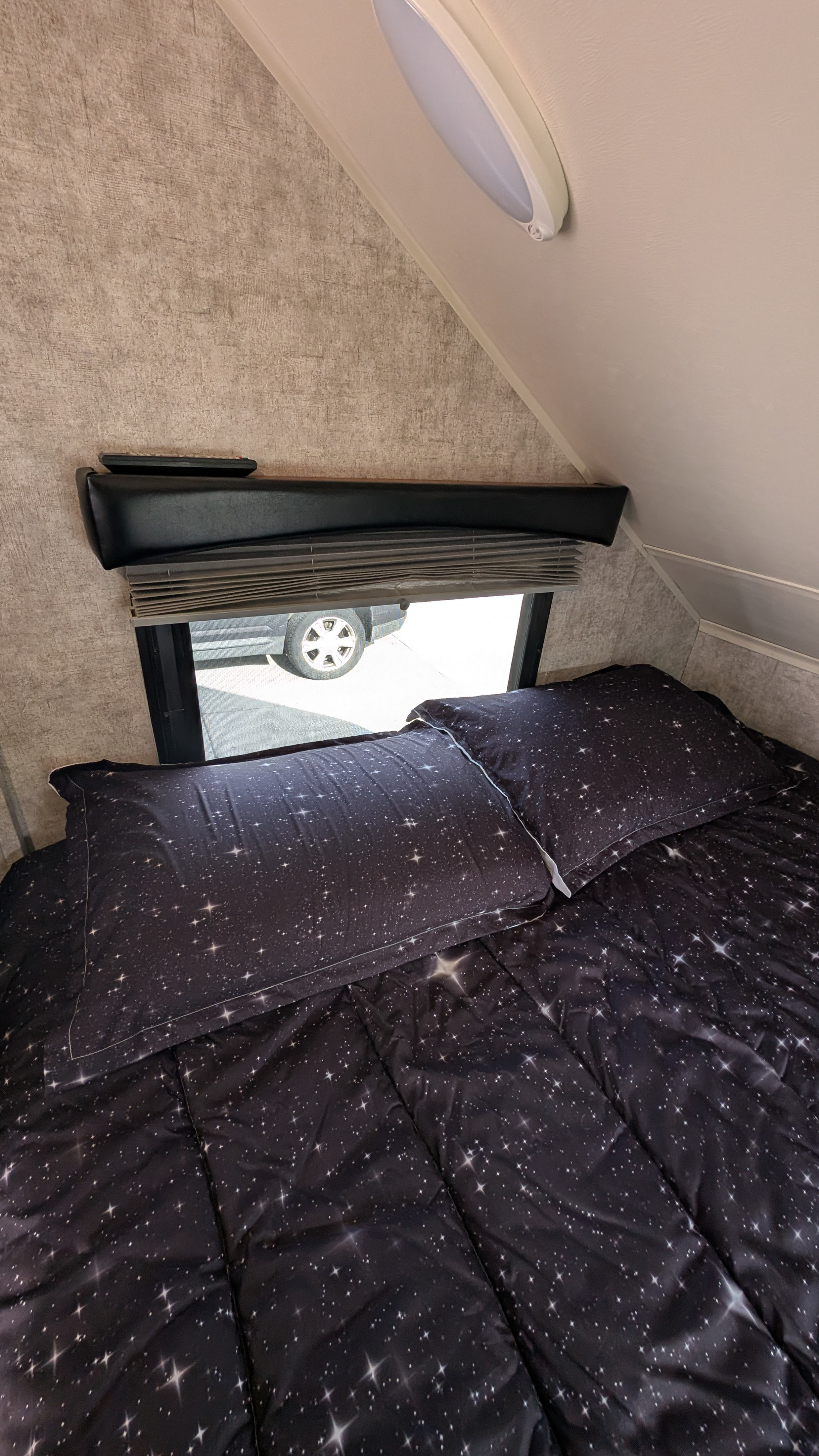 Starry bedspread in a cozy RV rental bedroom with window view, perfect for restful sleep.. Travel Lite Falcon 2018