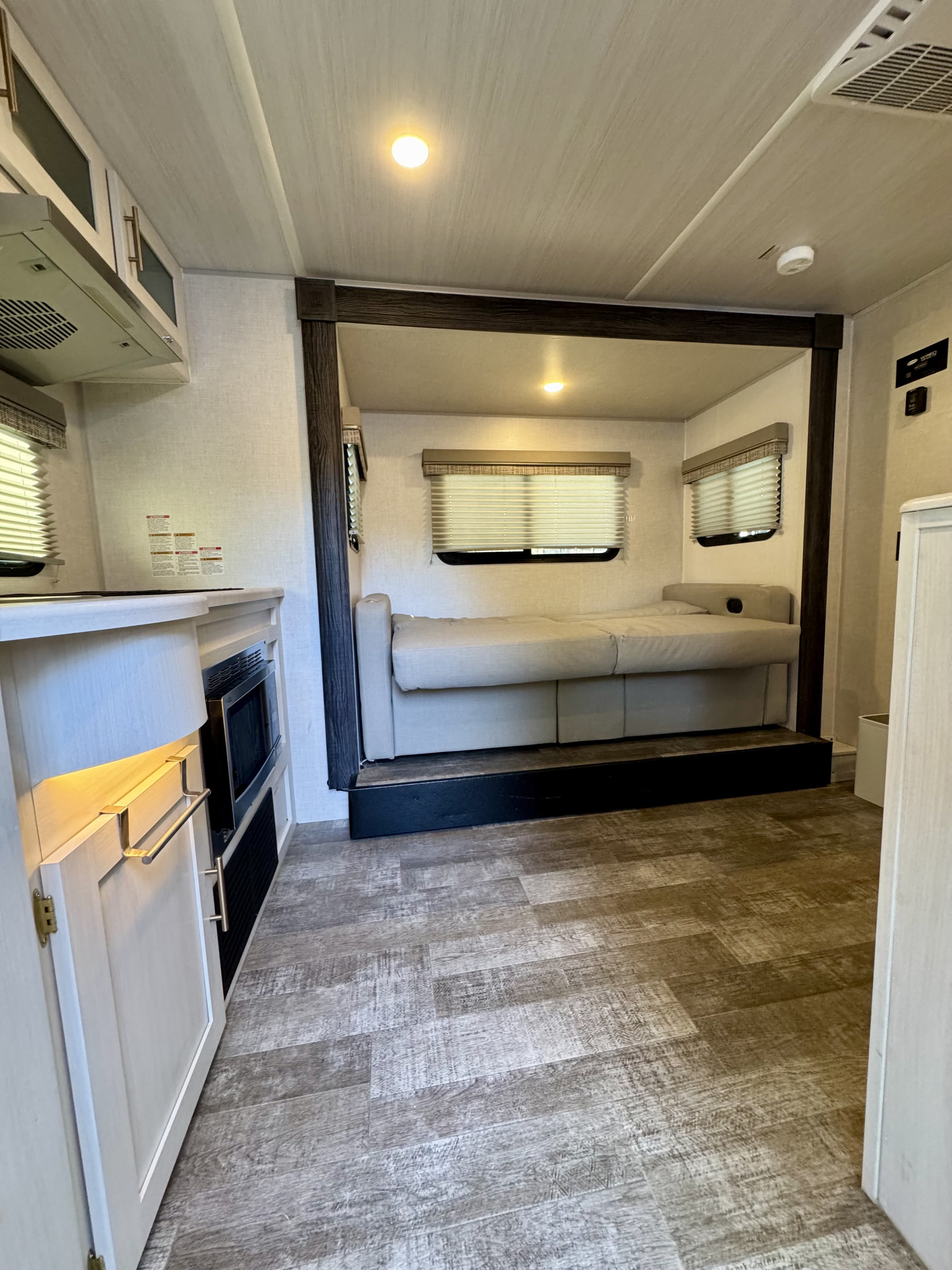 Spacious modern RV rental interior featuring a versatile bed/sofa, windows, kitchen area, and light wood-look flooring.. Forest River R-Pod RP-202 2022