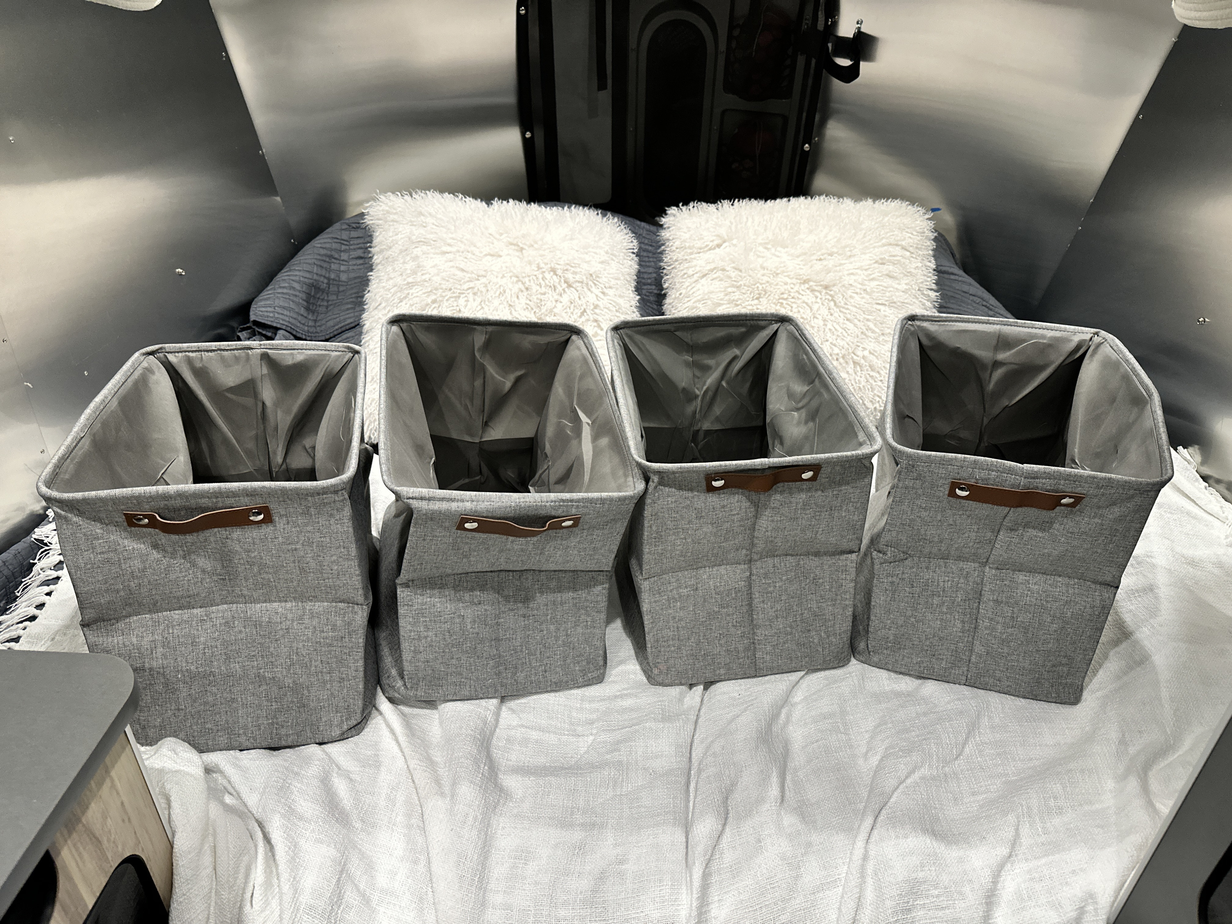 RV rental interior: organized bedroom with four grey storage bins, soft pillows, and a cozy bed.. Airstream Basecamp 2023