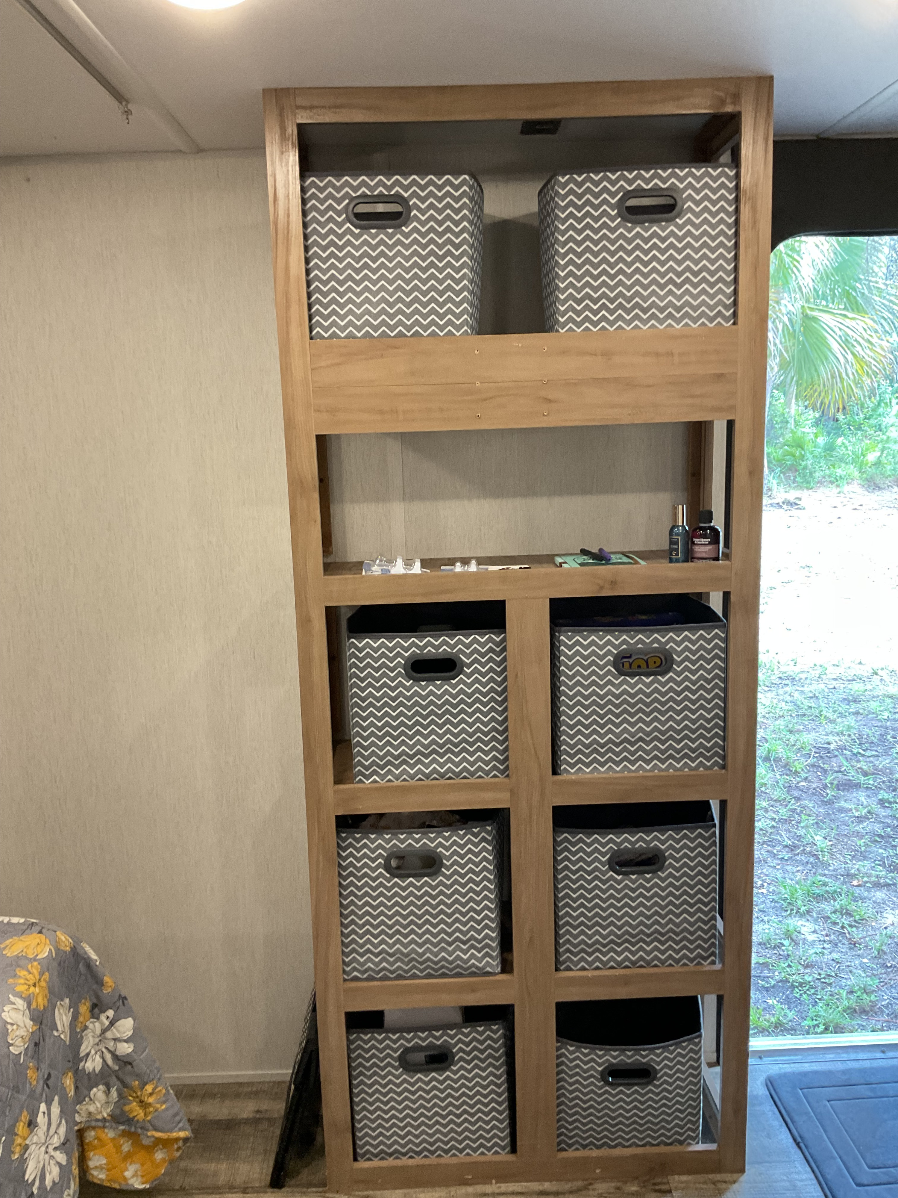 An RV rental interior features a tall wood shelving unit with grey chevron bins, maximizing storage.. Forest River Wolfden 26ev 2024