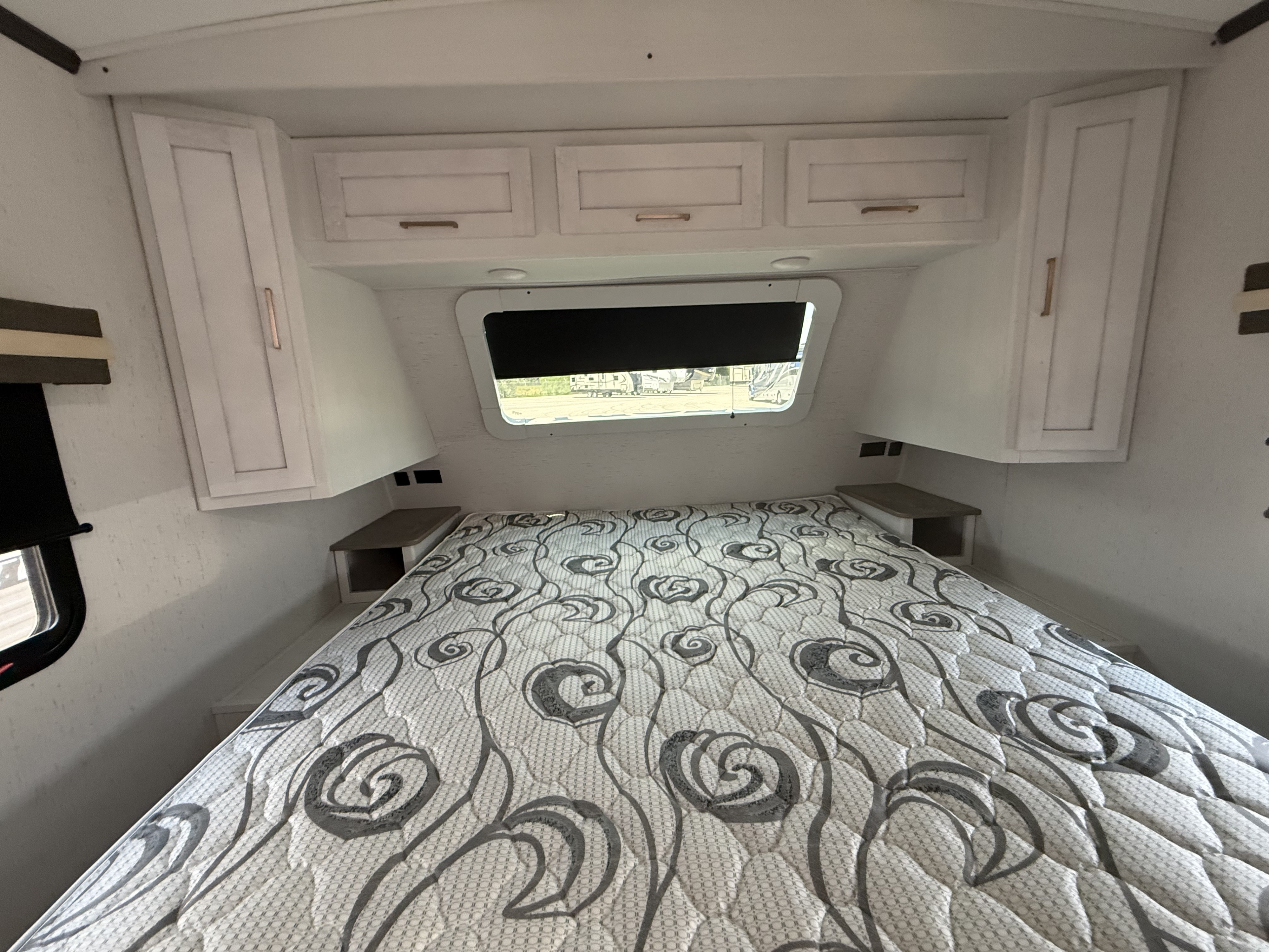 RV rental bedroom showcasing a comfortable bed with patterned mattress, overhead cabinets, and a window for natural light.. Astoria Astoria Trailer 2022