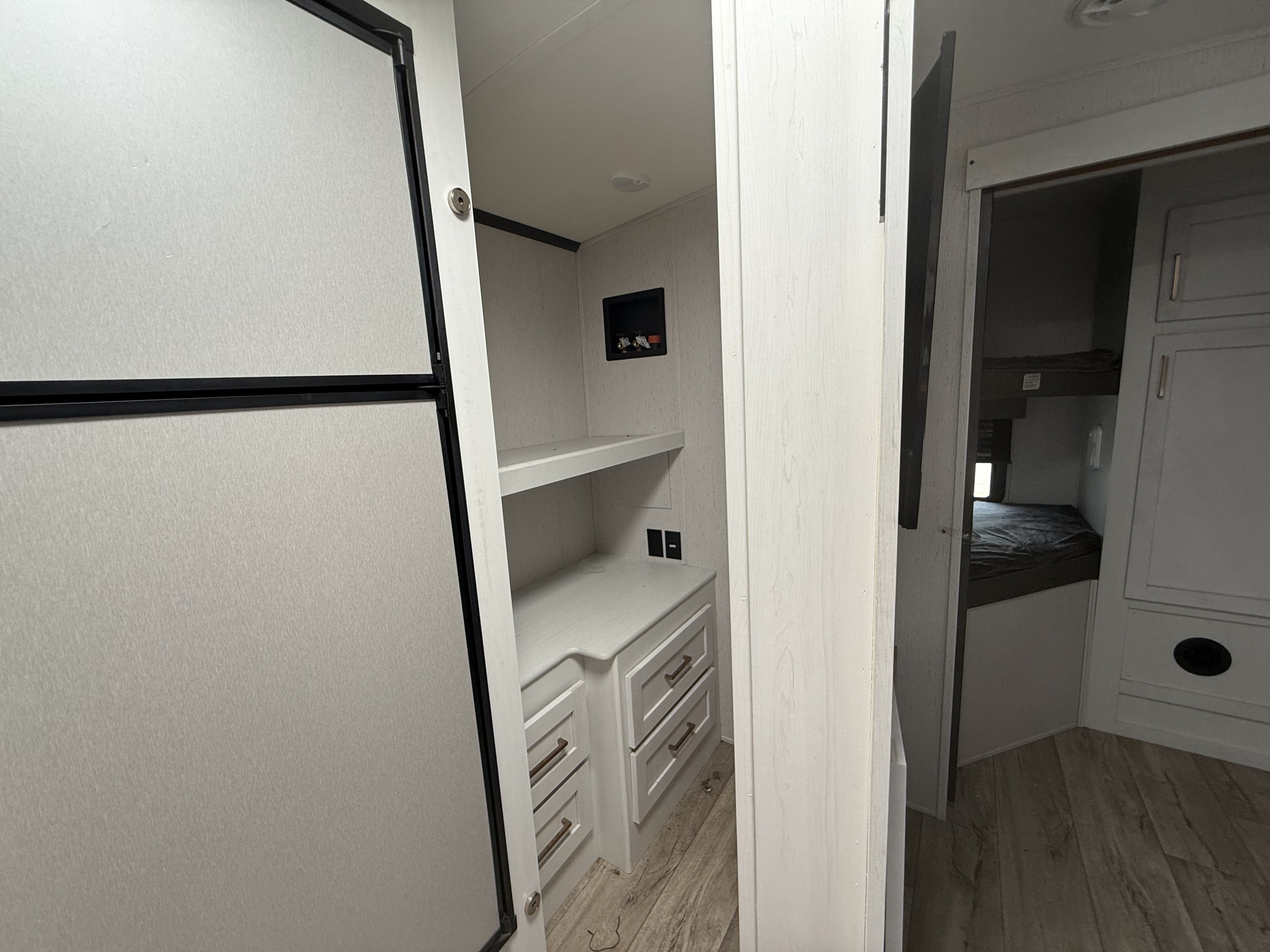 Inside an RV rental, showing a fridge, built-in storage, laundry hookups, and a glimpse of the bunk beds. Modern and functional.. Astoria Astoria Trailer 2022