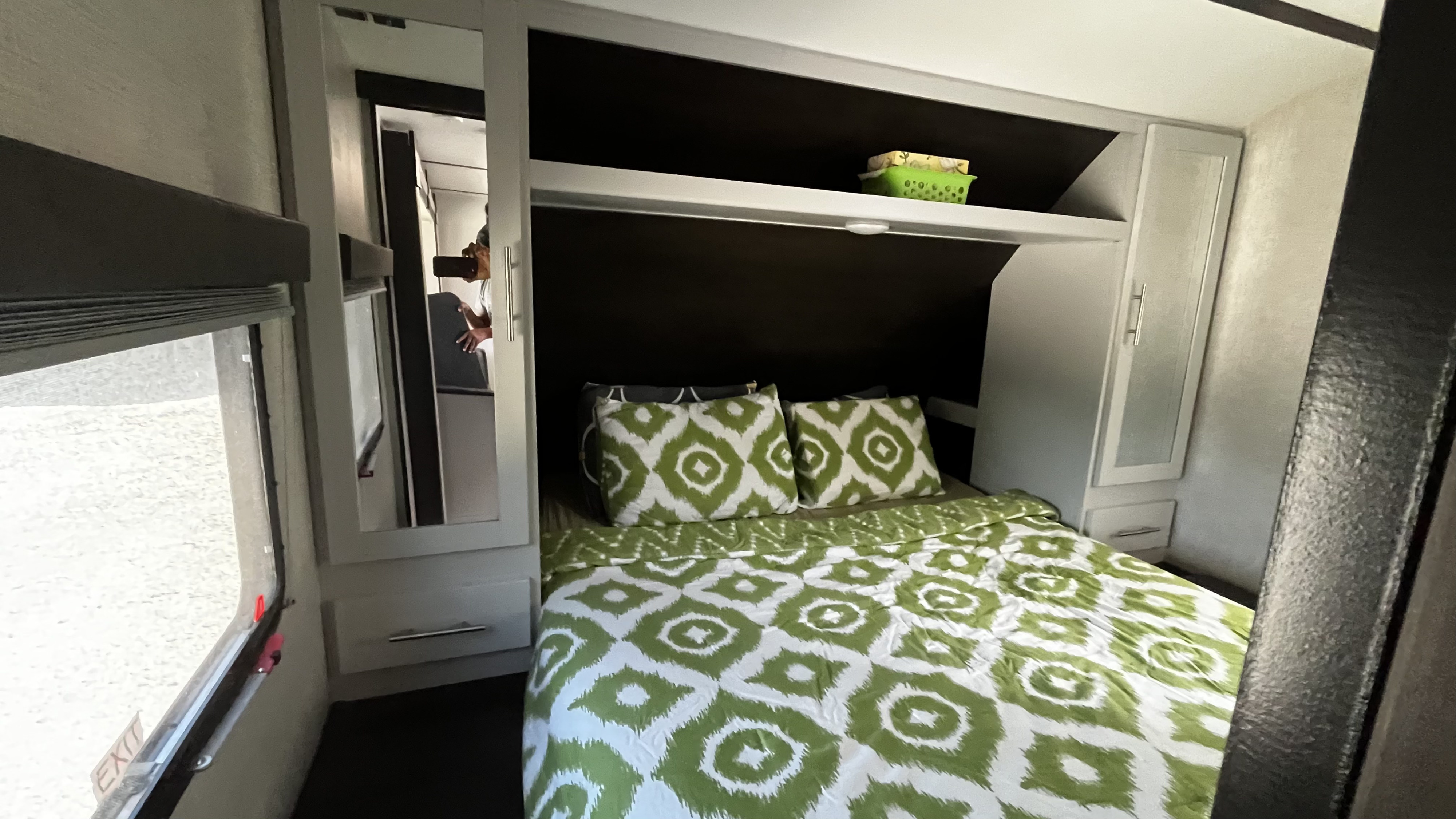 Cozy RV rental bedroom featuring green patterned bedding, ample built-in storage, and a mirrored cabinet.. Keystone RV Bullet Ultra Lite 2020