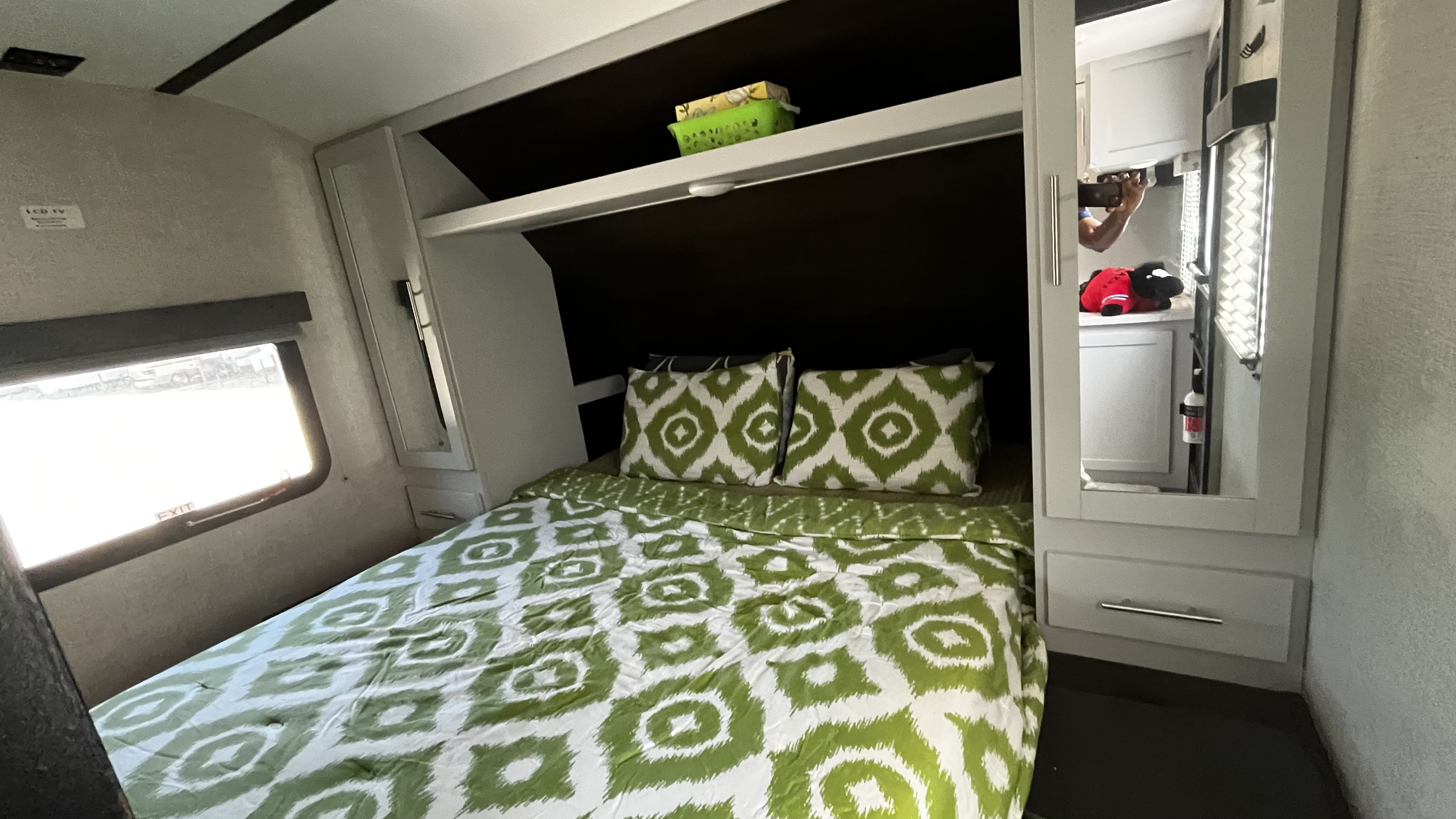 Cozy RV rental bedroom featuring a bed with green and white patterned bedding, overhead storage, and a window.. Keystone RV Bullet Ultra Lite 2020