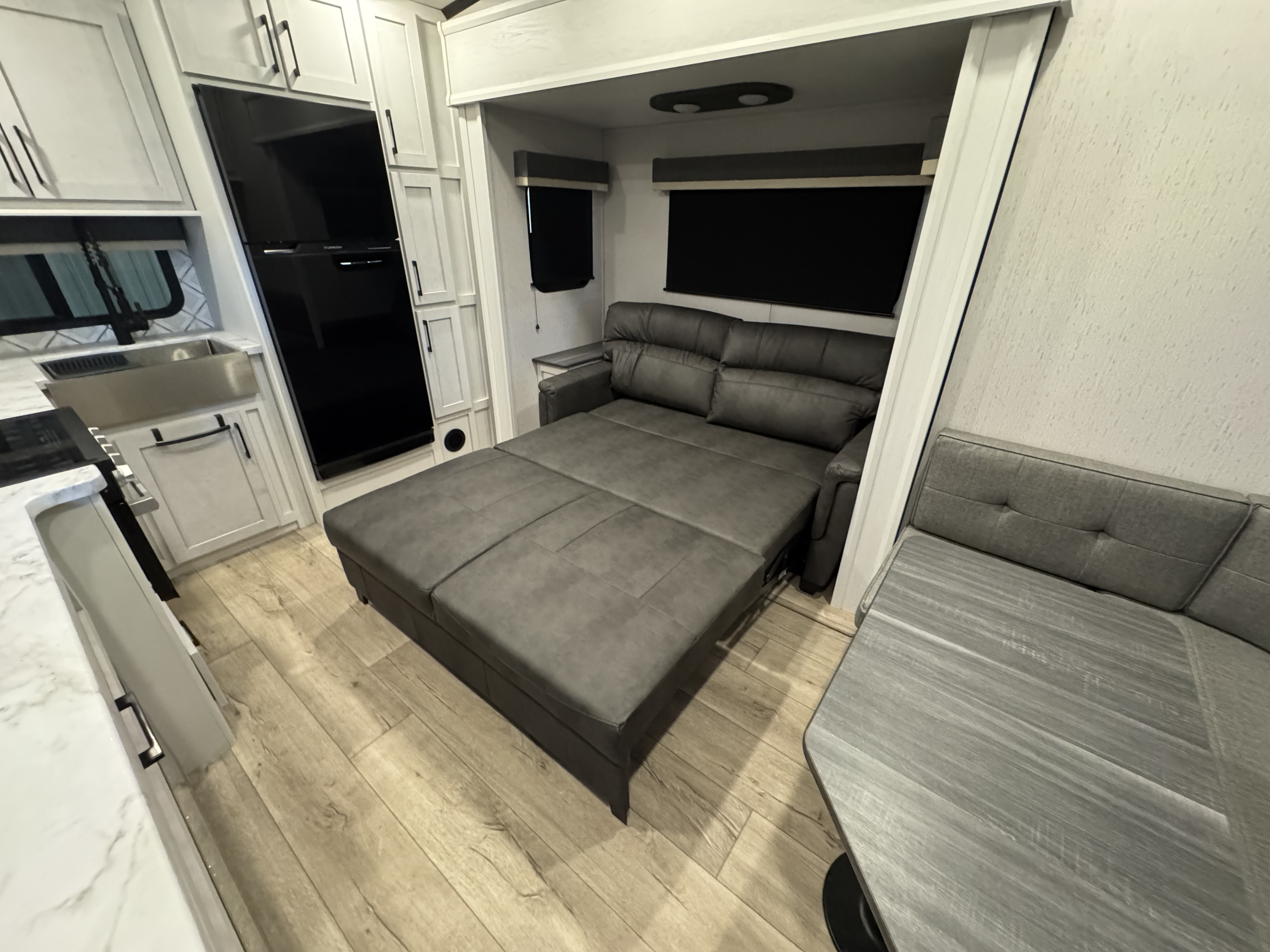 Spacious modern RV rental interior: kitchen with fridge, extended sofa bed, and dining area on light wood floor.. Dutchmen Astoria 260RK 2025