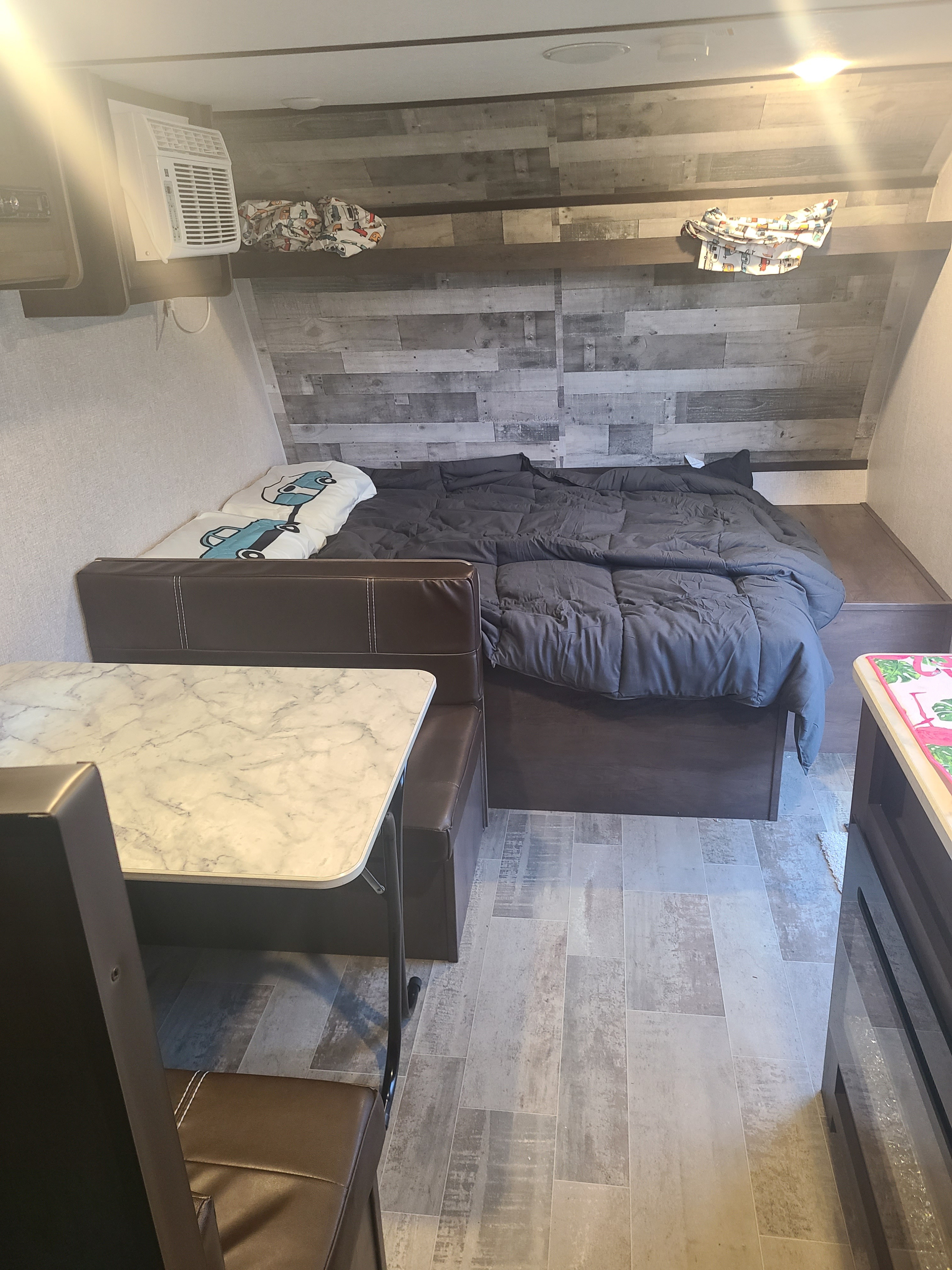 Inside an RV rental: a comfortable bed with gray bedding, a practical dinette with a marble-look table, and an AC unit.. Dutchmen Coleman Lantern LT 2021