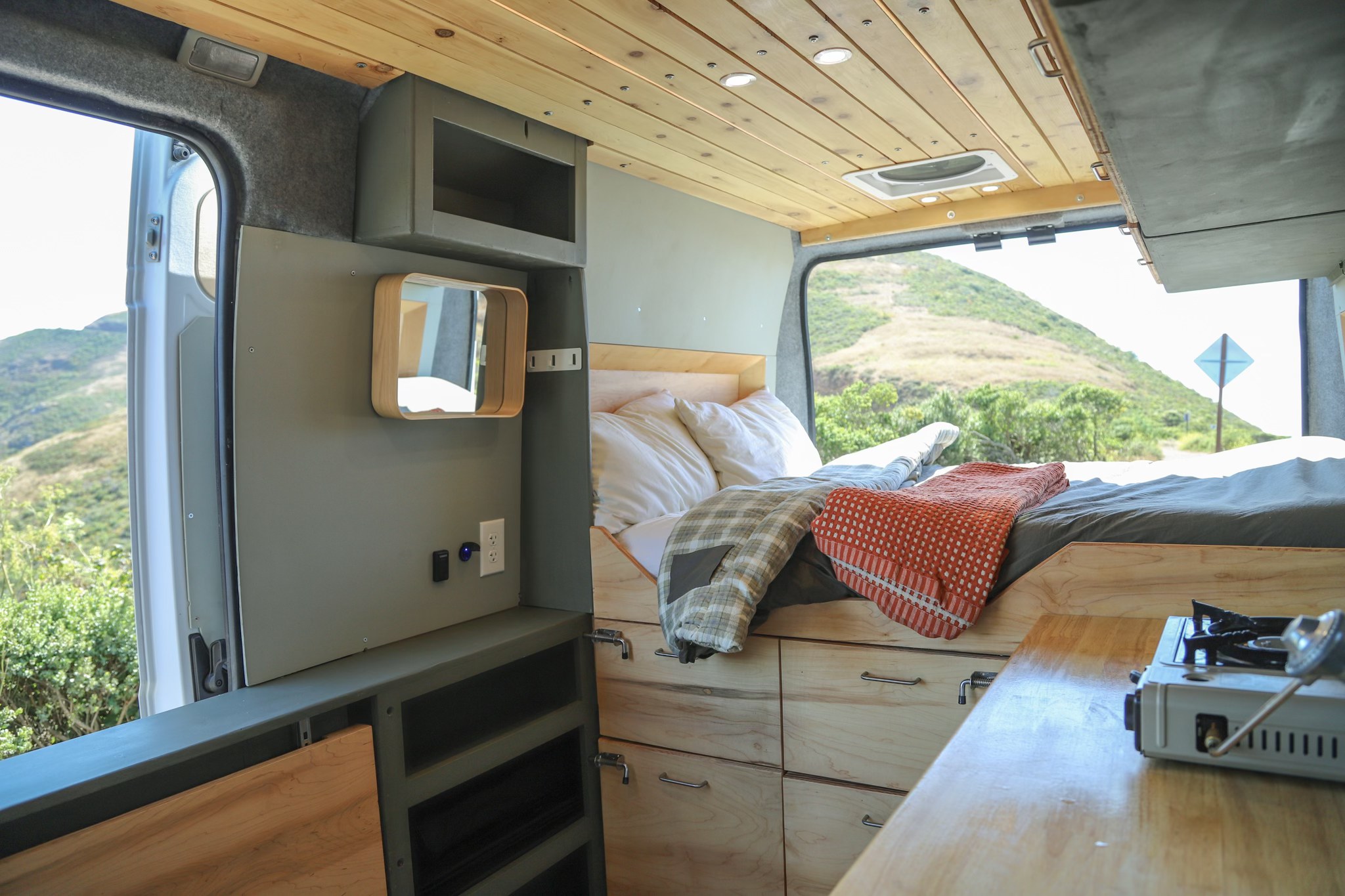 Experience van life! This RV rental features a cozy bed, kitchen space with stove, & scenic views out the open doors.. Dodge Ram Promaster 2023