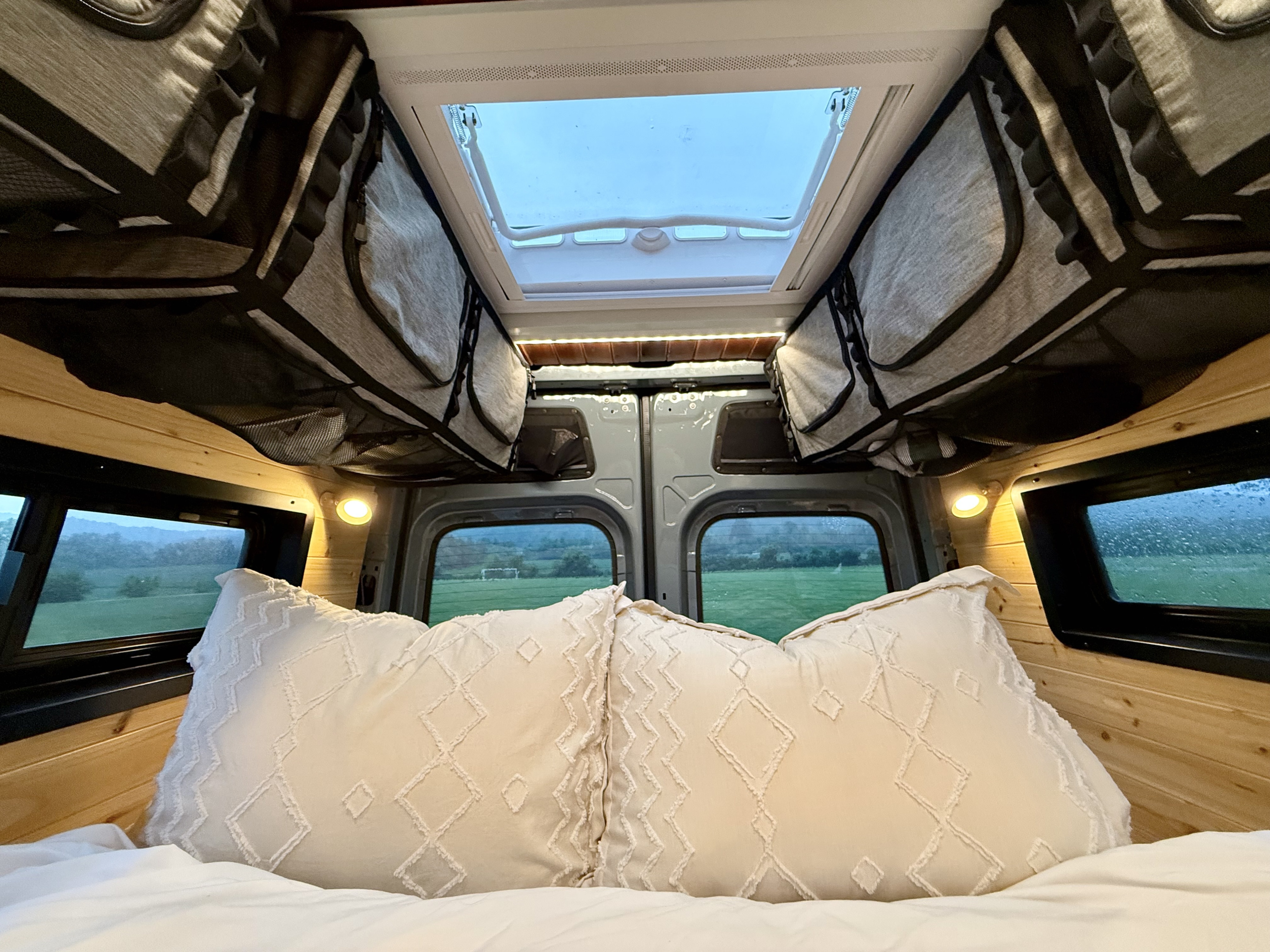 Cozy RV rental interior: bed with pillows, wood walls, skylight, and scenic view from the back.. MERCEDES-BENZ SPRINTER 2500 170 WB 2022