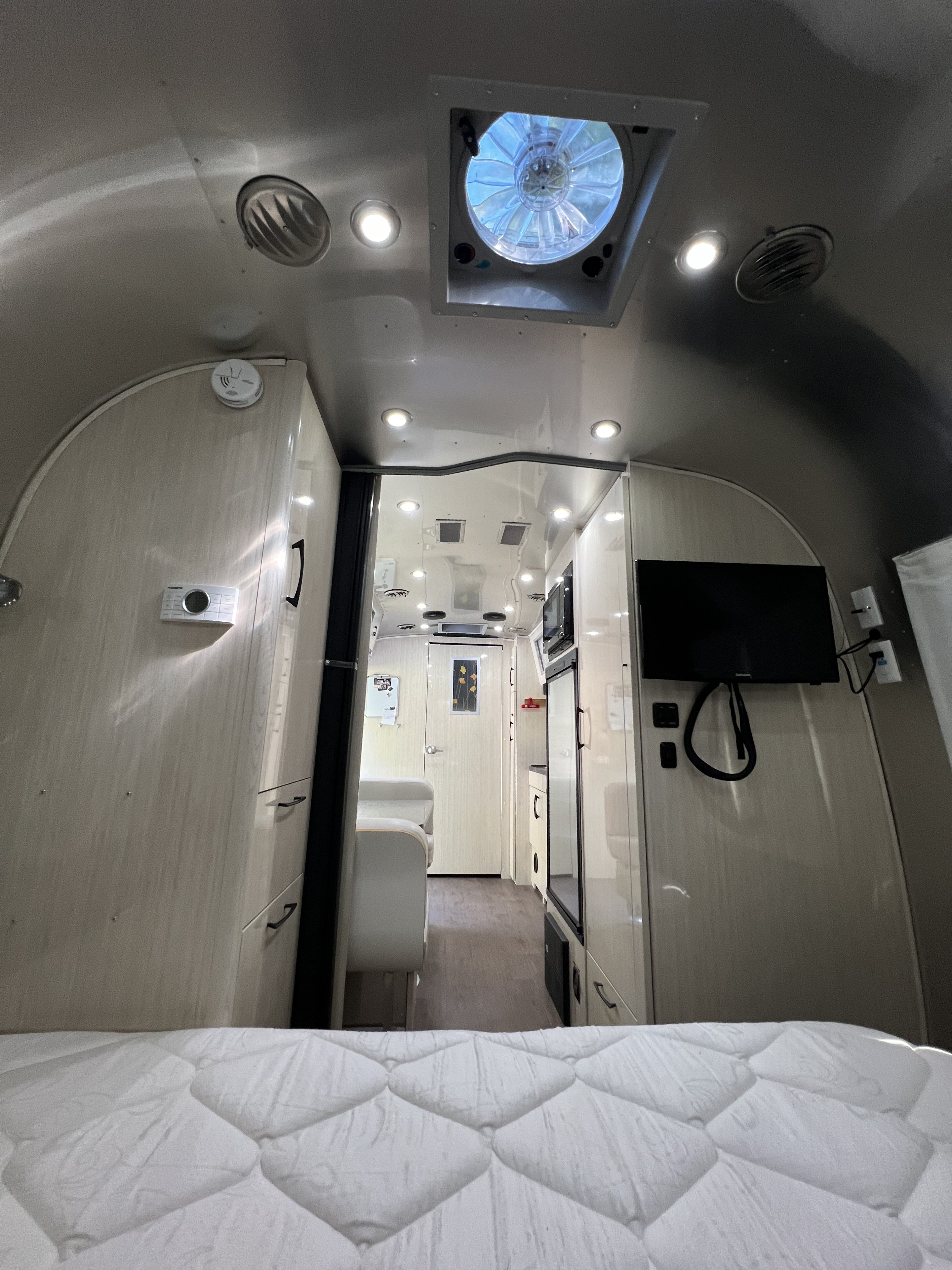 View inside an RV rental. From the bed, looking through the galley with a ceiling fan, TV, and light wood cabinetry.. Airstream International 2018