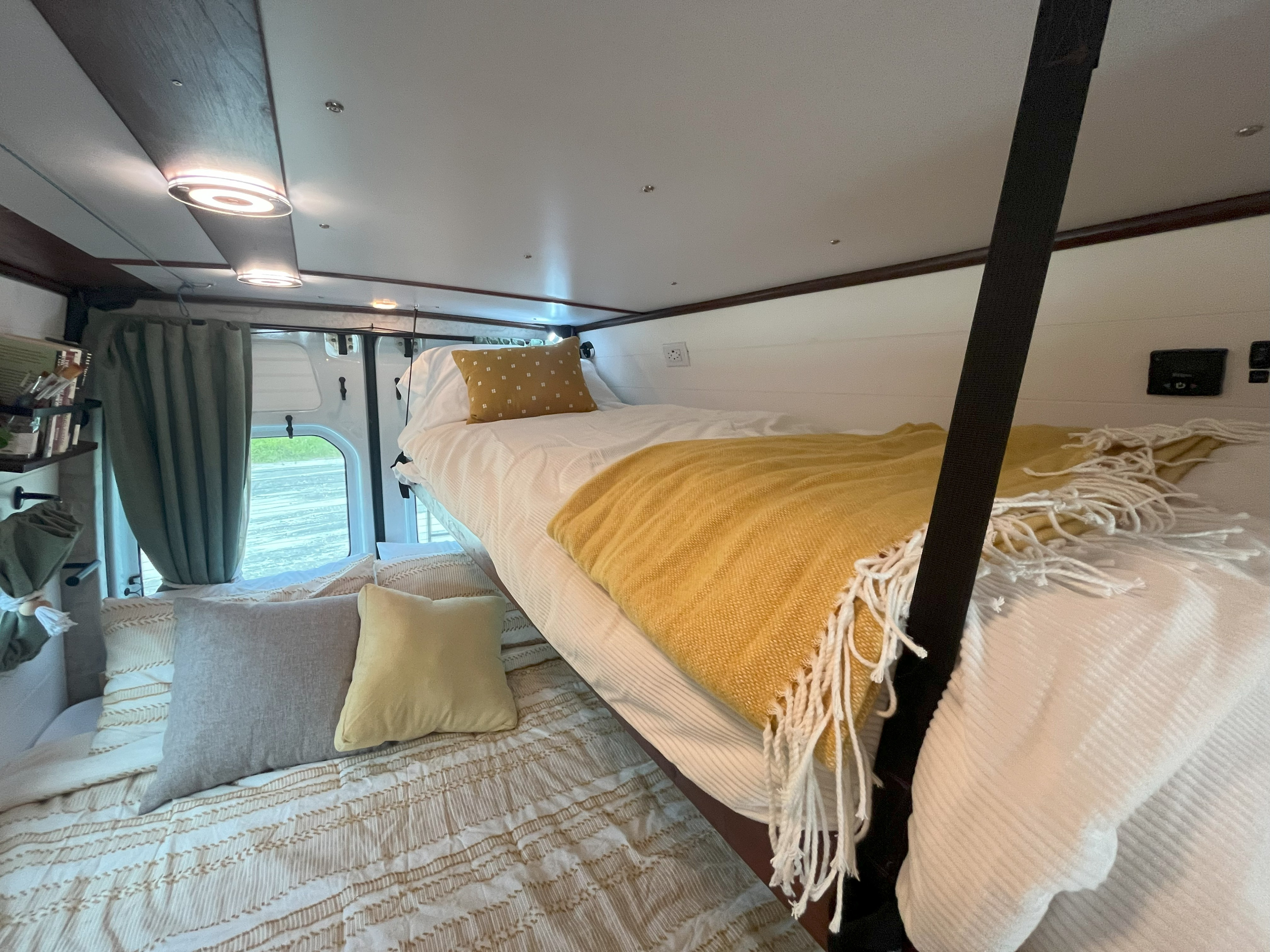 Interior of an RV rental showing cozy bunk beds, complete with bright blankets and pillows, ideal for a camper van stay.. Mercedes-Benz Sprinter 2015
