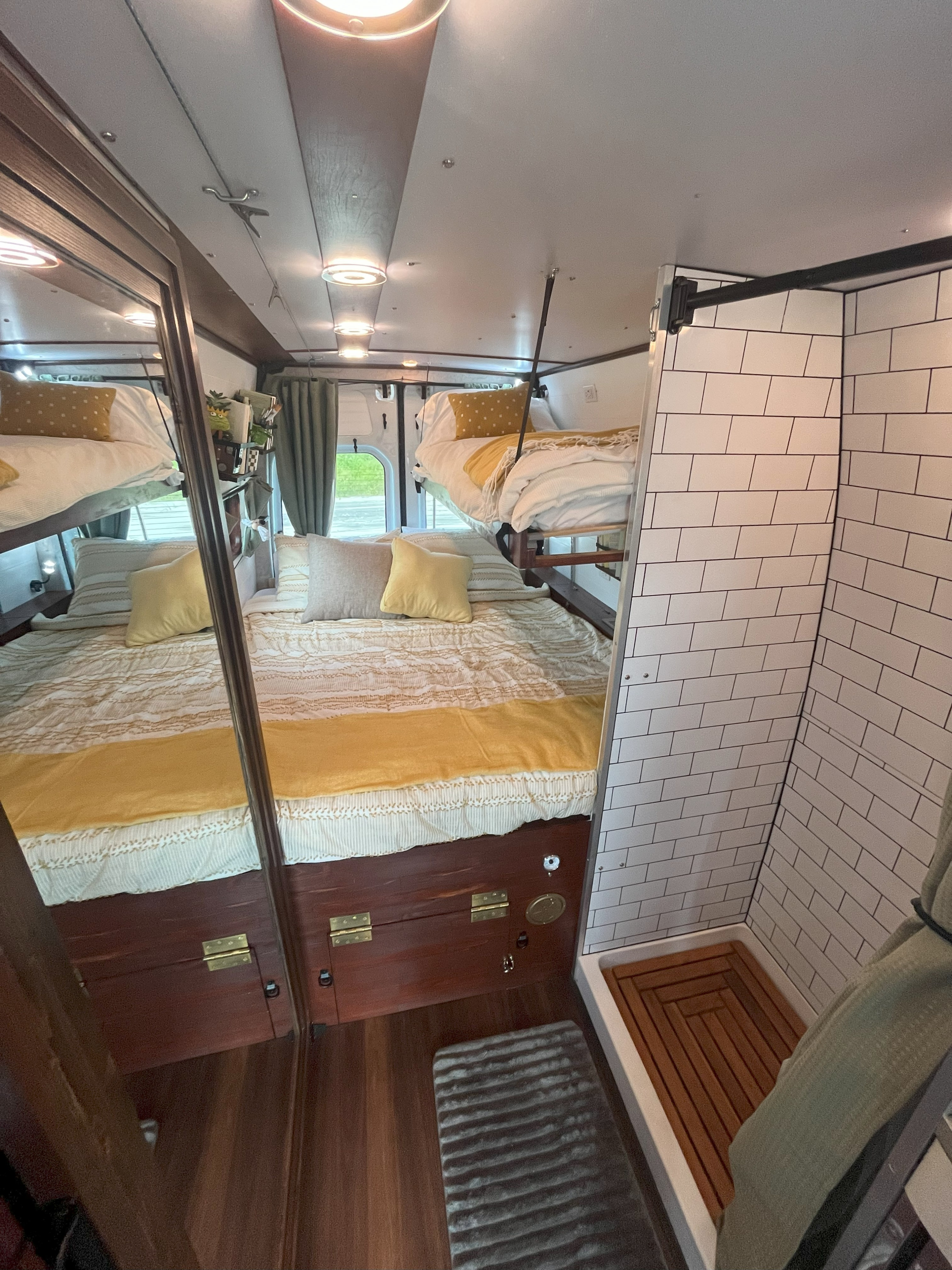 Cozy rv rental interior with a main bed, fold-down bunk, and compact tiled shower. Perfect for road trips.. Mercedes-Benz Sprinter 2015
