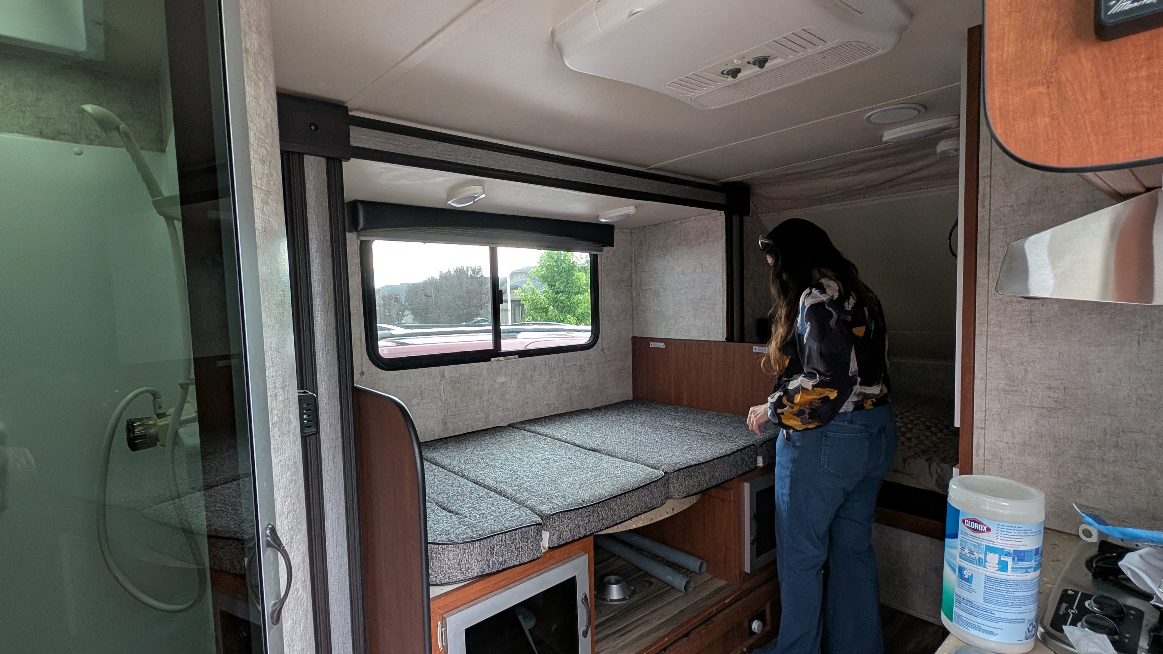 An RV rental's adaptable interior: a woman stands near the convertible bed, with a full shower to the left.. Travel Lite Falcon 2018