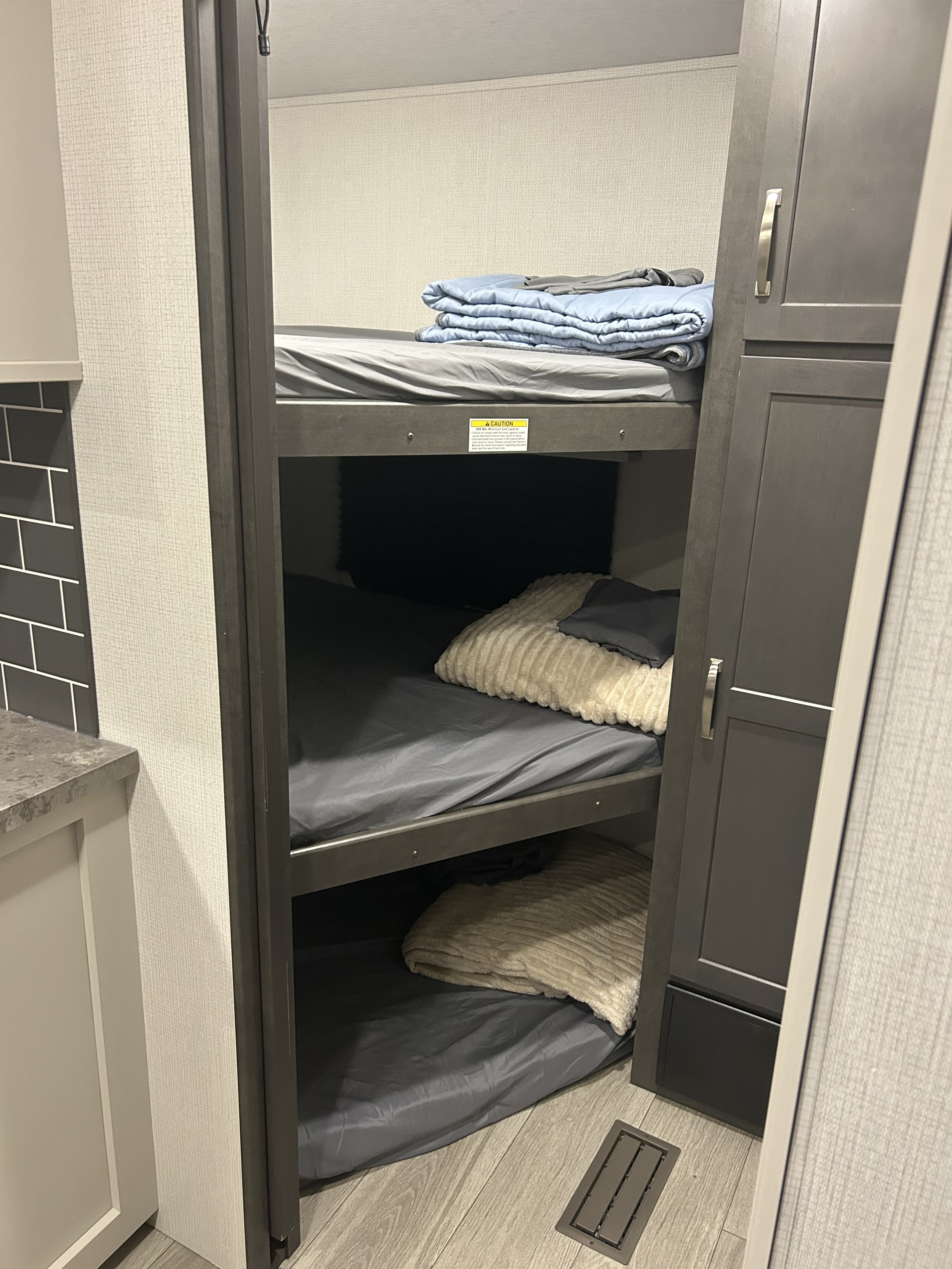 Triple bunk beds in a modern RV rental, featuring cozy bedding, smart storage, and a floor vent.. Keystone Cougar 2025