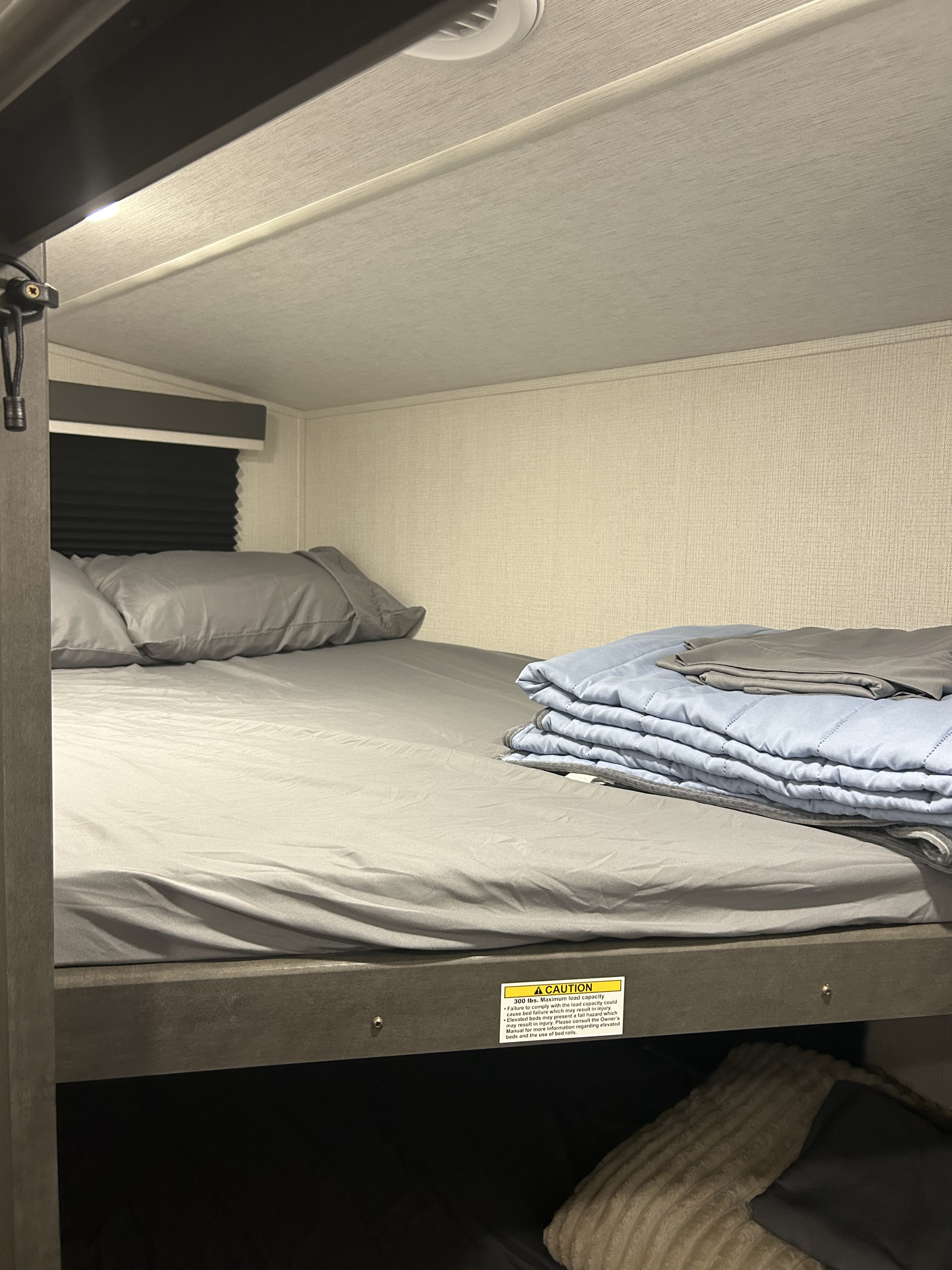 Exploring an RV rental: a cozy bunk bed, complete with gray bedding and a folded blue blanket for travel.. Keystone Cougar 2025