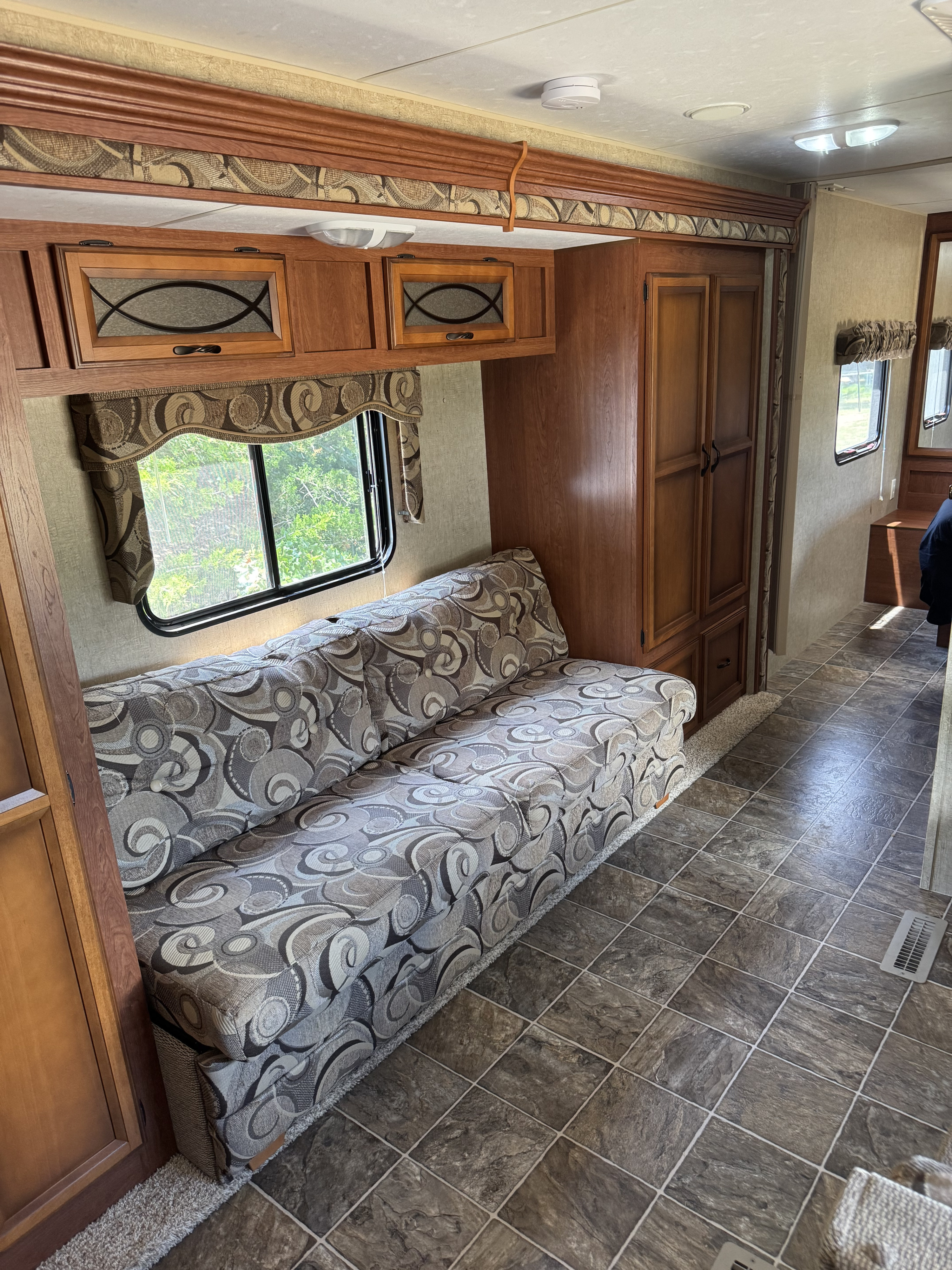 This clean RV rental interior features a patterned sofa, overhead wood cabinets, a large window, and durable tiled floor.. Sportsmen Sportsmen Trailer 2013