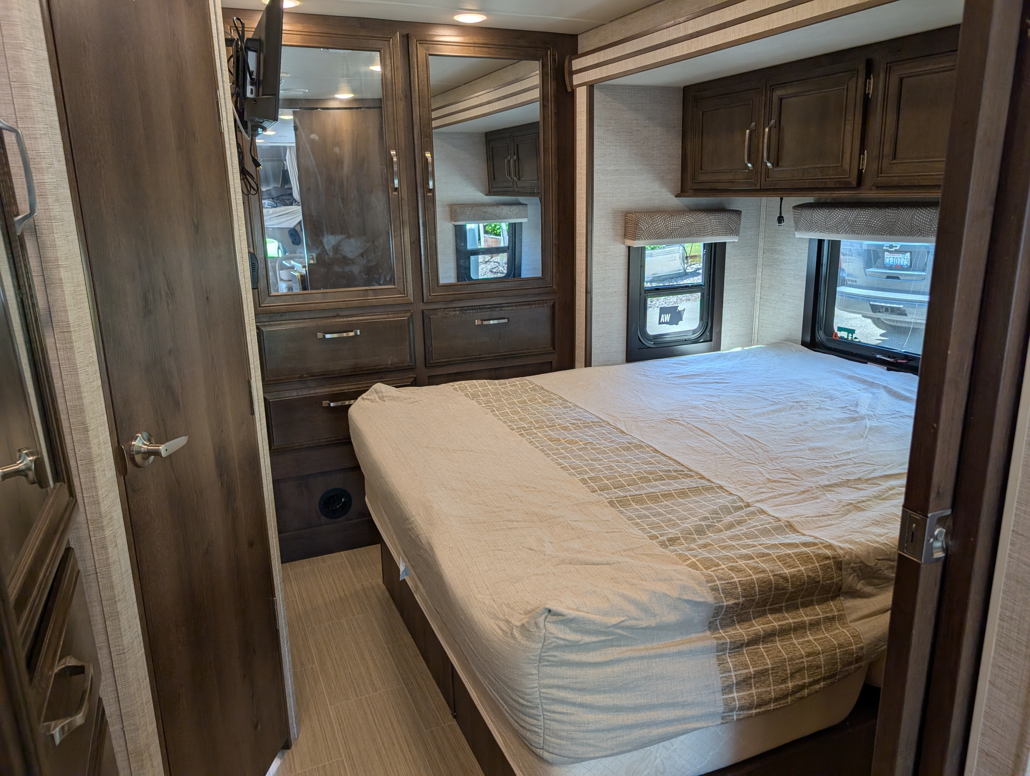Spacious RV rental bedroom with a comfortable bed, mirrored storage, TV, and bright windows for your trip.. Entegra Coach Esteem 2021