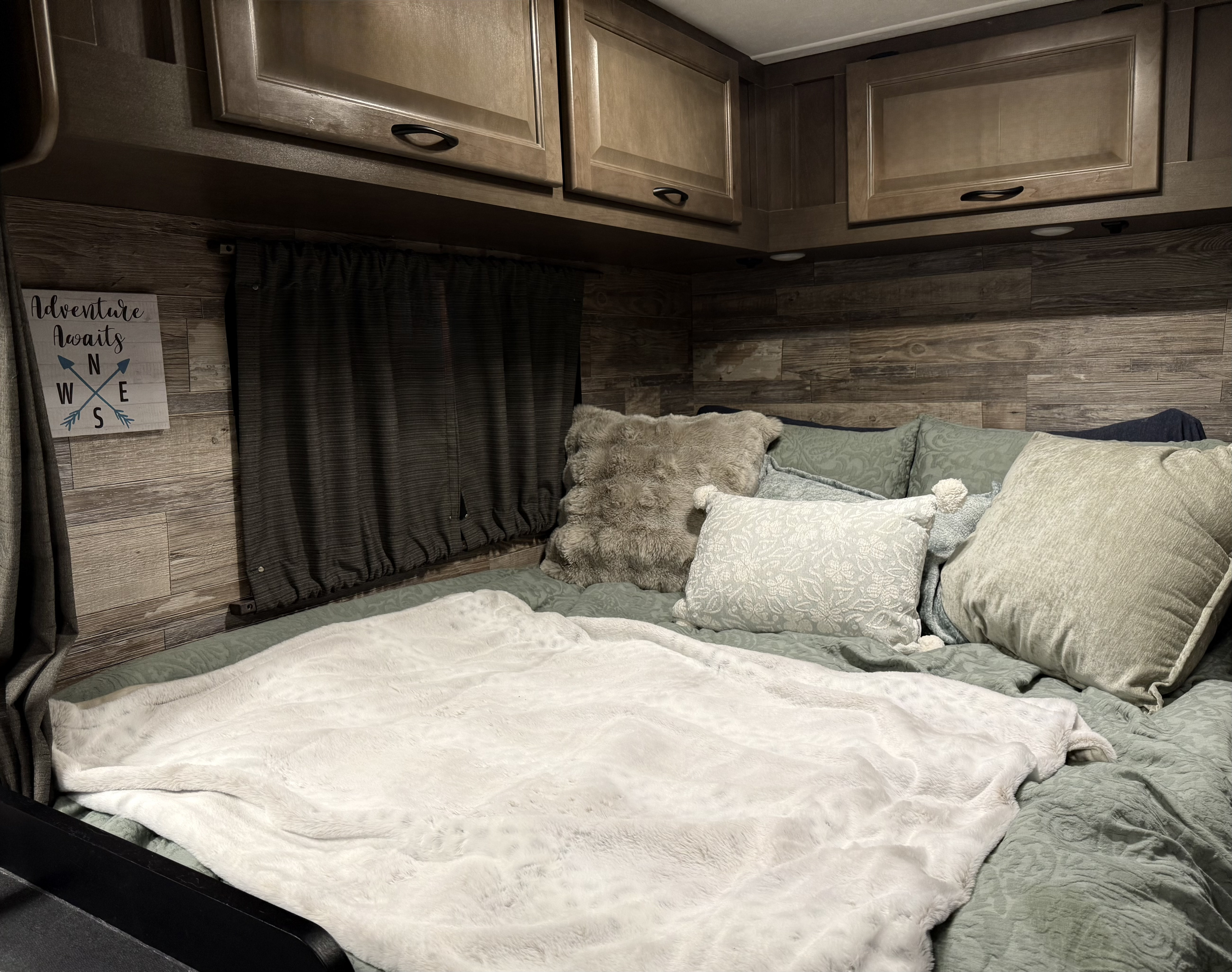 Cozy RV rental bedroom with warm wood paneling, comfy bed, and "Adventure Awaits" decor.. Thor Majestic 2019
