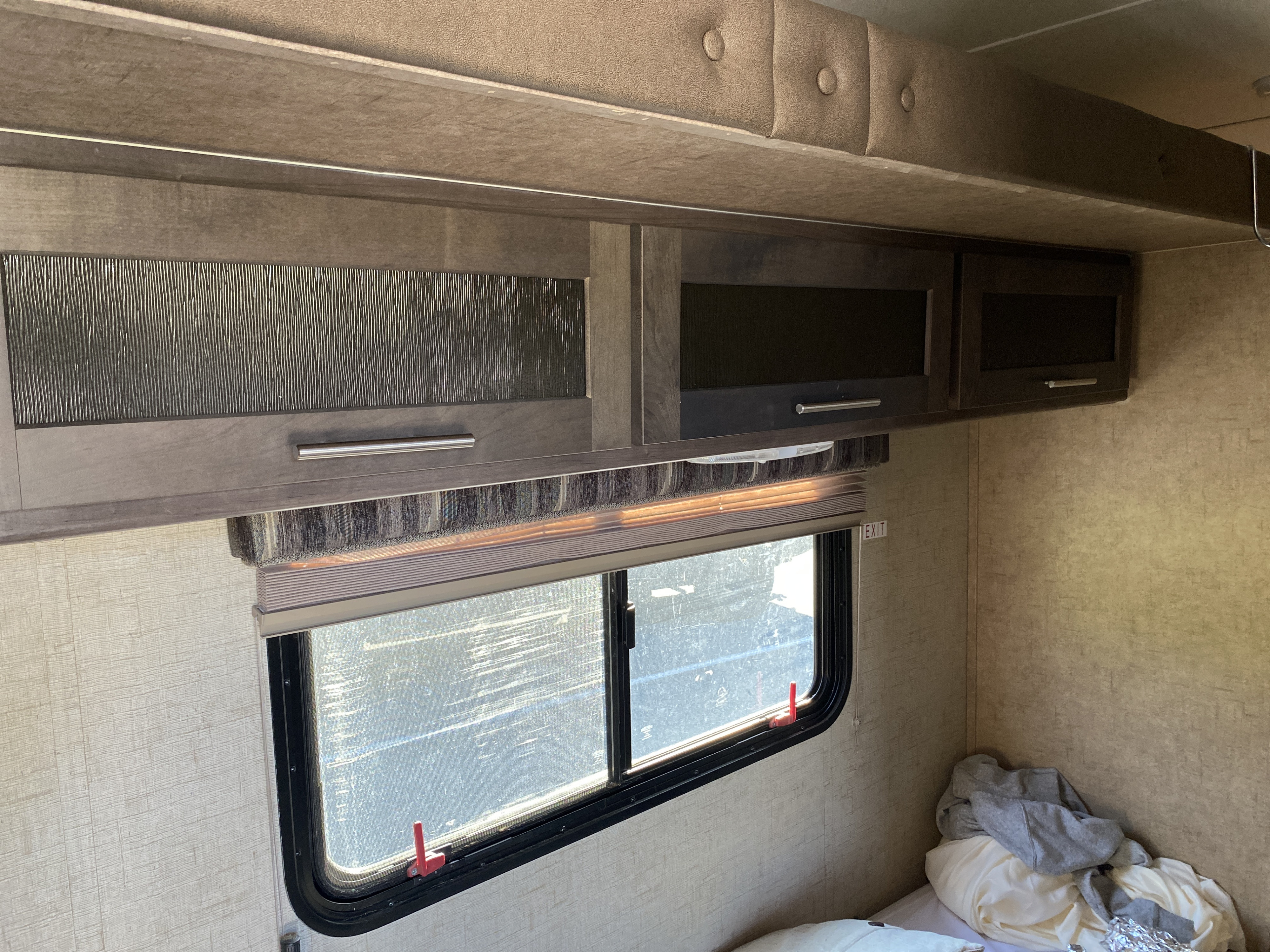 RV rental interior view: Overhead dark wood cabinets, some textured, over a window with blinds, and a bed in the sleeping area.. R-Pod R-Pod Trailer 2015