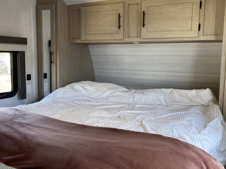 Cozy RV rental bedroom: light wood shiplap, overhead cabinets, white patterned bed with brown blanket. Your comfy retreat!. Forest River Wildwood Lodge 2023