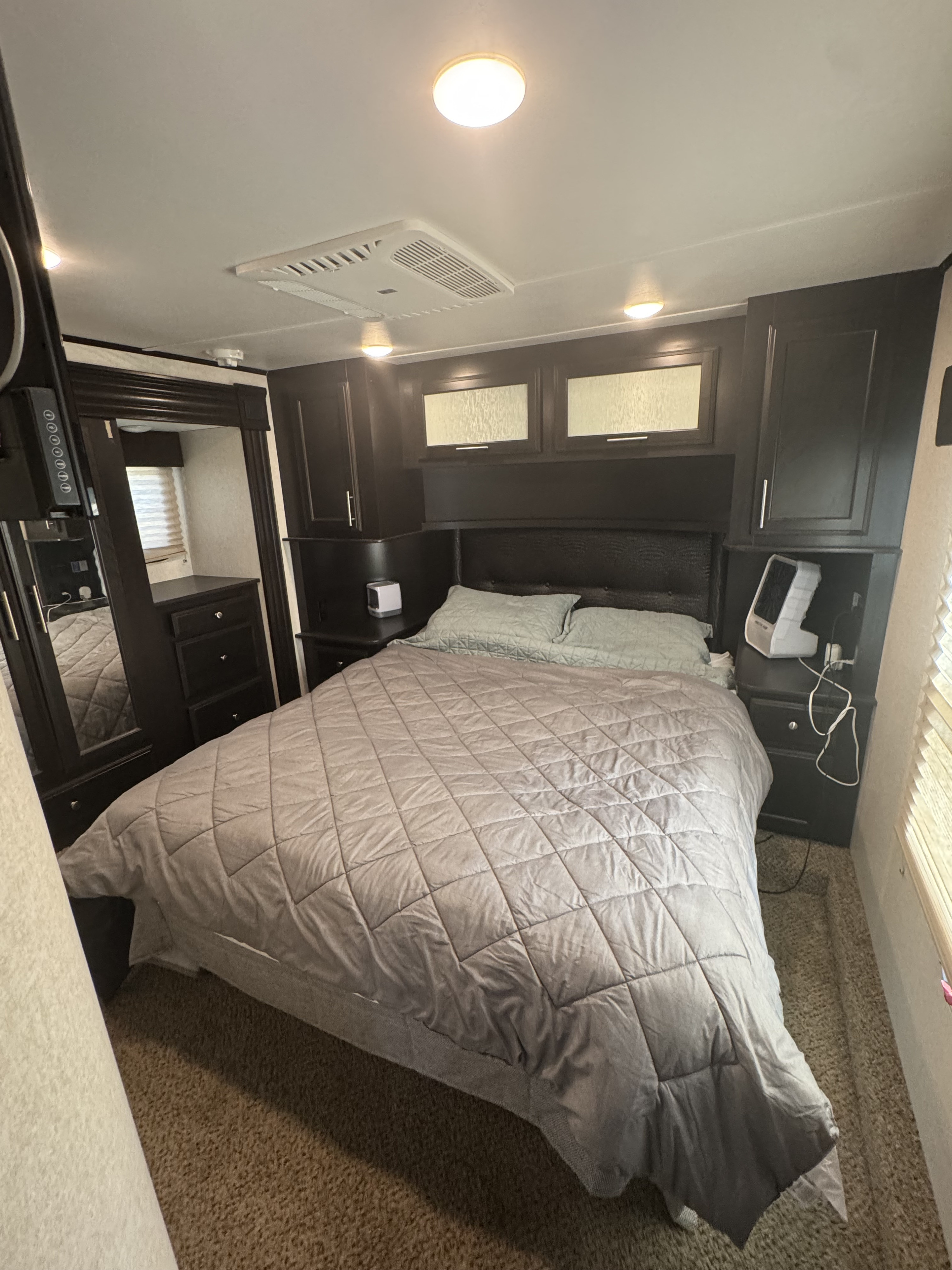 An RV rental bedroom with a bed, dark wood cabinetry, integrated storage, nightstands, AC unit, and lights on the ceiling.. Jayco Seismic Toy Hauler 2017