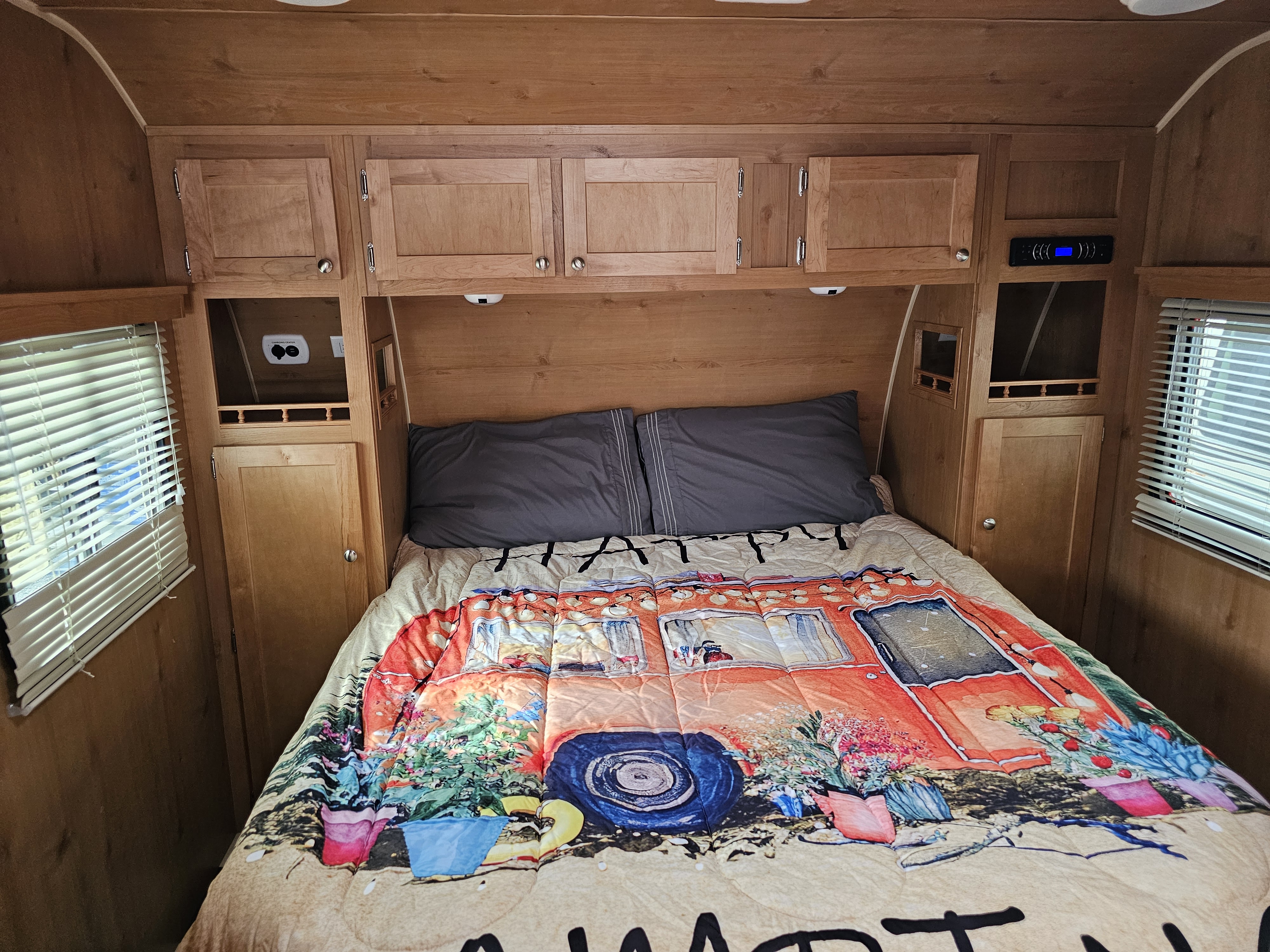 Inside a cozy RV rental bedroom: wooden paneling, bed with vibrant camper comforter, overhead cabinets & amenities.. Riverside RV 195 White Water 2016