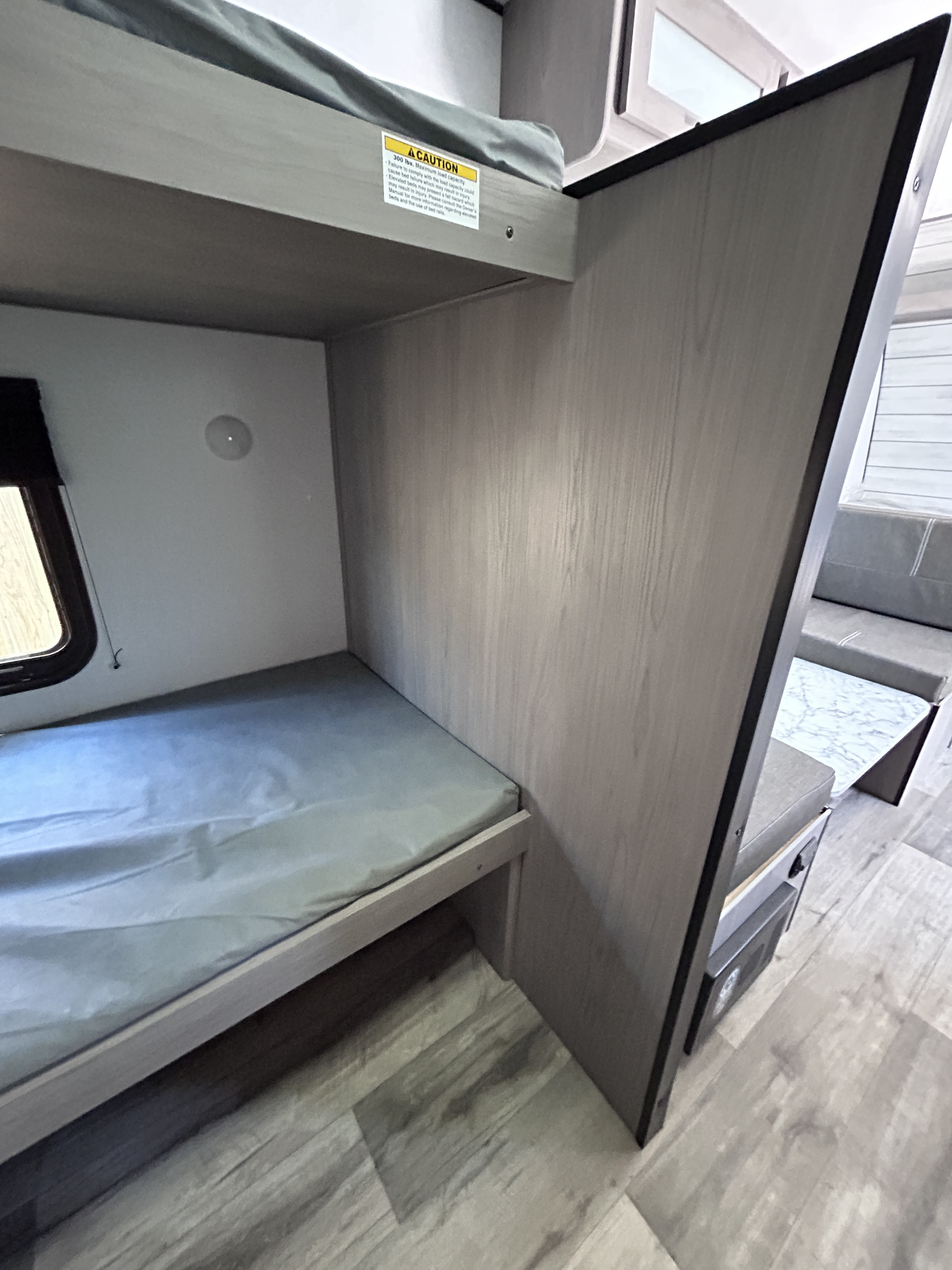 Bunk beds & a dinette in an rv rental, featuring gray mattresses. Top bunk has a 300lb capacity warning.. Dutchmen Coleman 2024