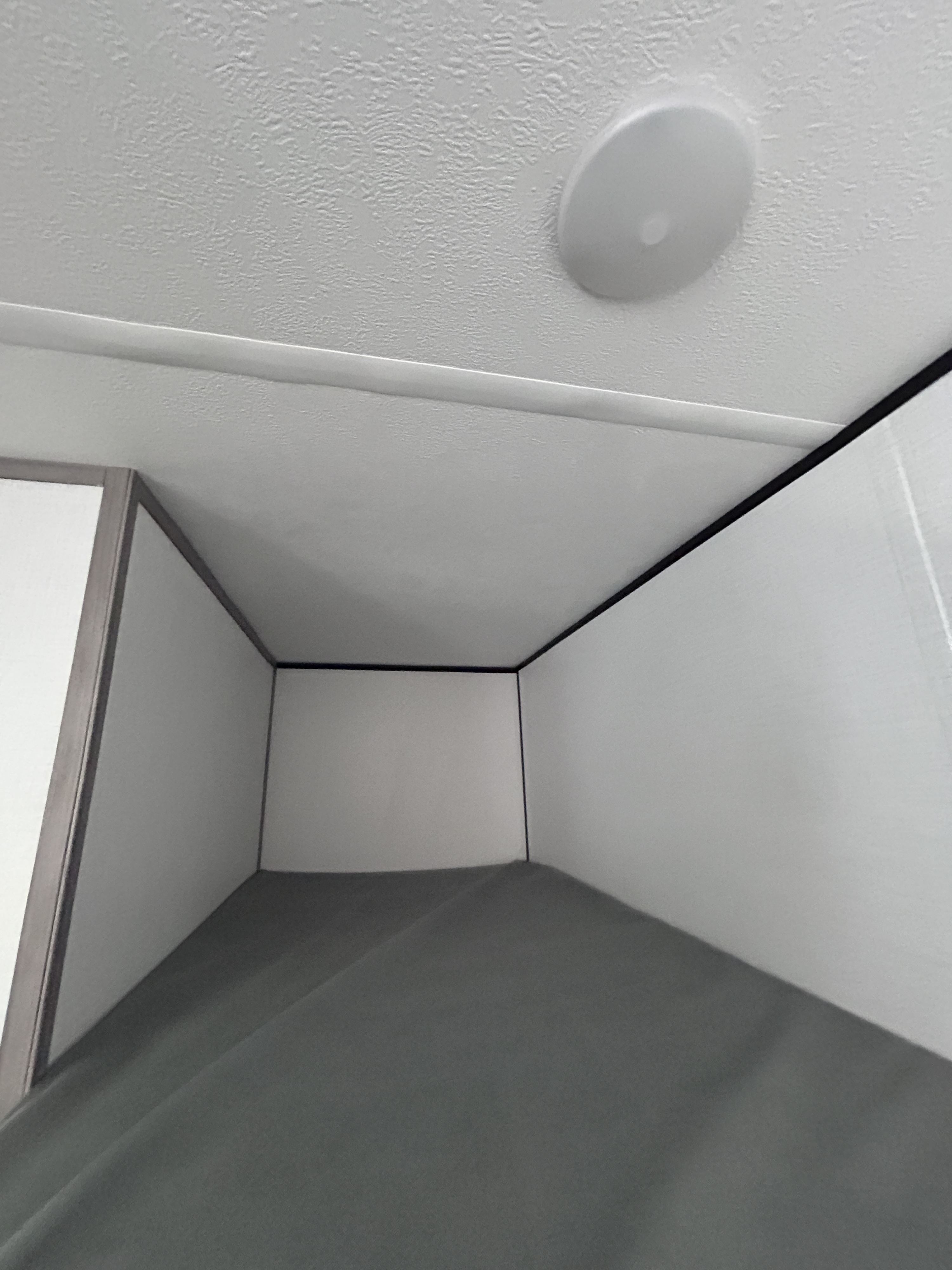 RV rental interior showing a compact sleeping bunk with white walls, dark trim, and a grey mattress, plus a ceiling light.. Dutchmen Coleman 2024