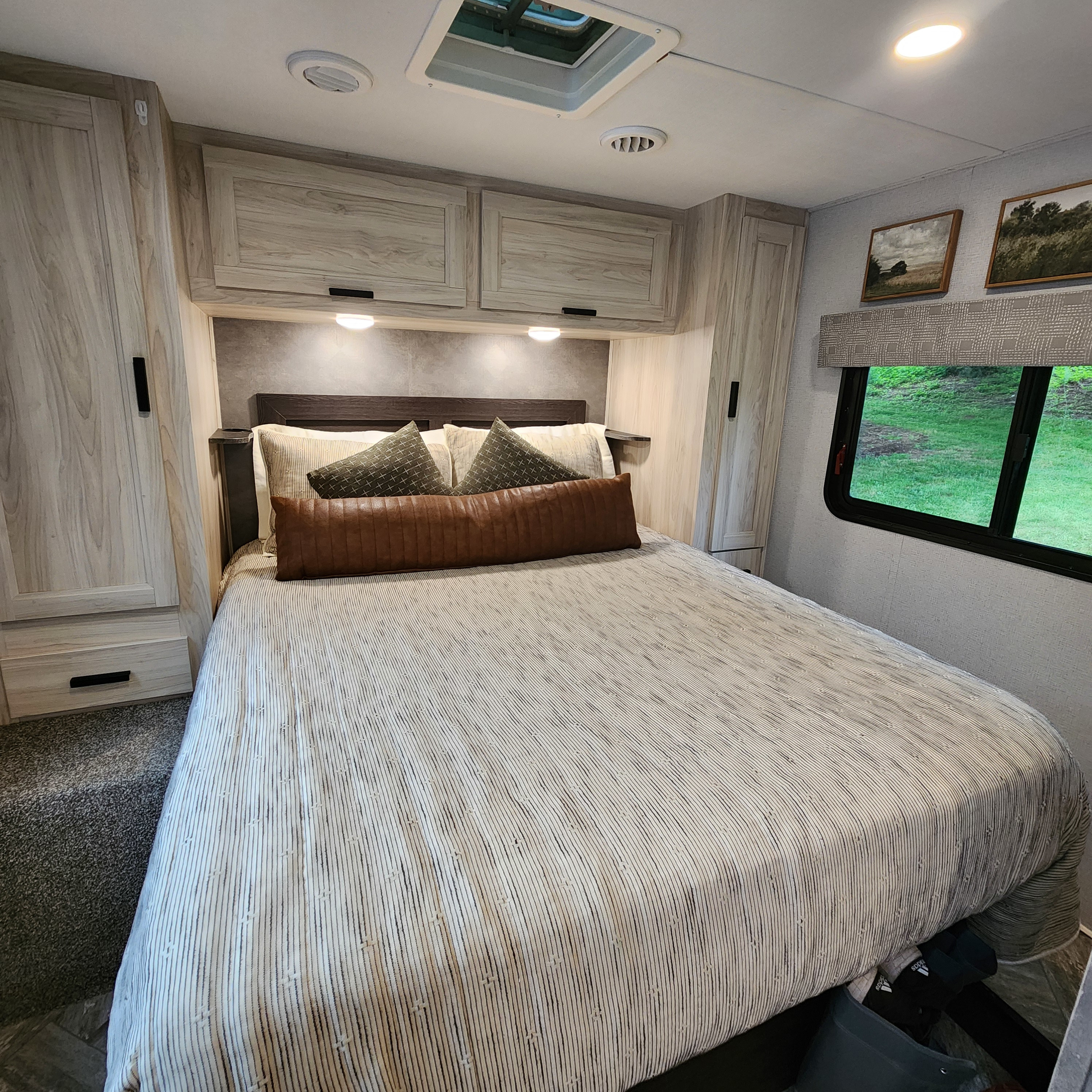 Modern RV rental bedroom. Features light wood cabinetry, a comfy bed with striped comforter, and scenic window views.. Forest River Sunseeker LE 2022