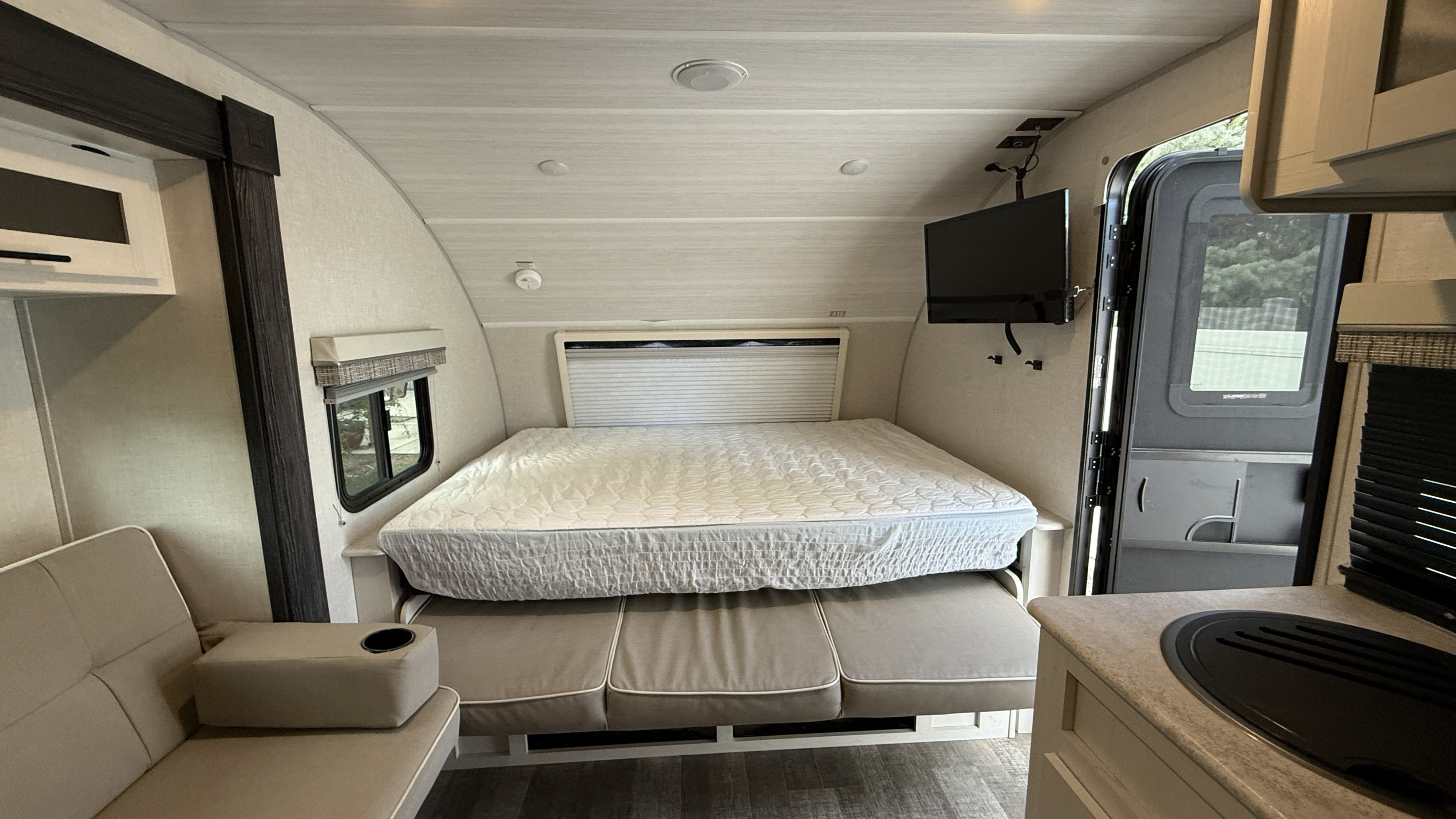 An RV rental interior showcasing a fold-down bed above a sofa, a compact kitchen area, and a wall-mounted TV.. R-Pod R-Pod Trailer 2022