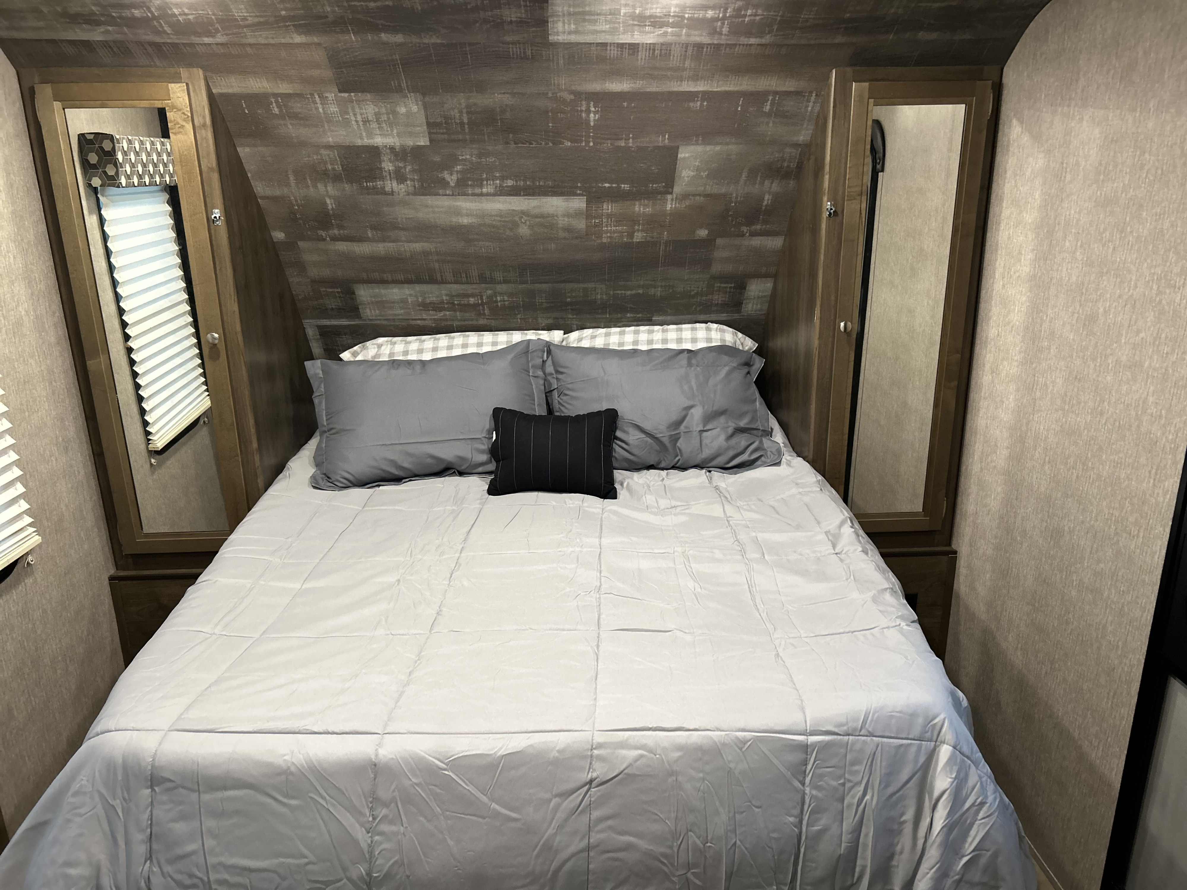 RV rental bedroom: a comfortable bed with gray bedding, flanked by mirrored cabinets and wood-paneled walls.. Dutchmen Coleman Light LX 2020